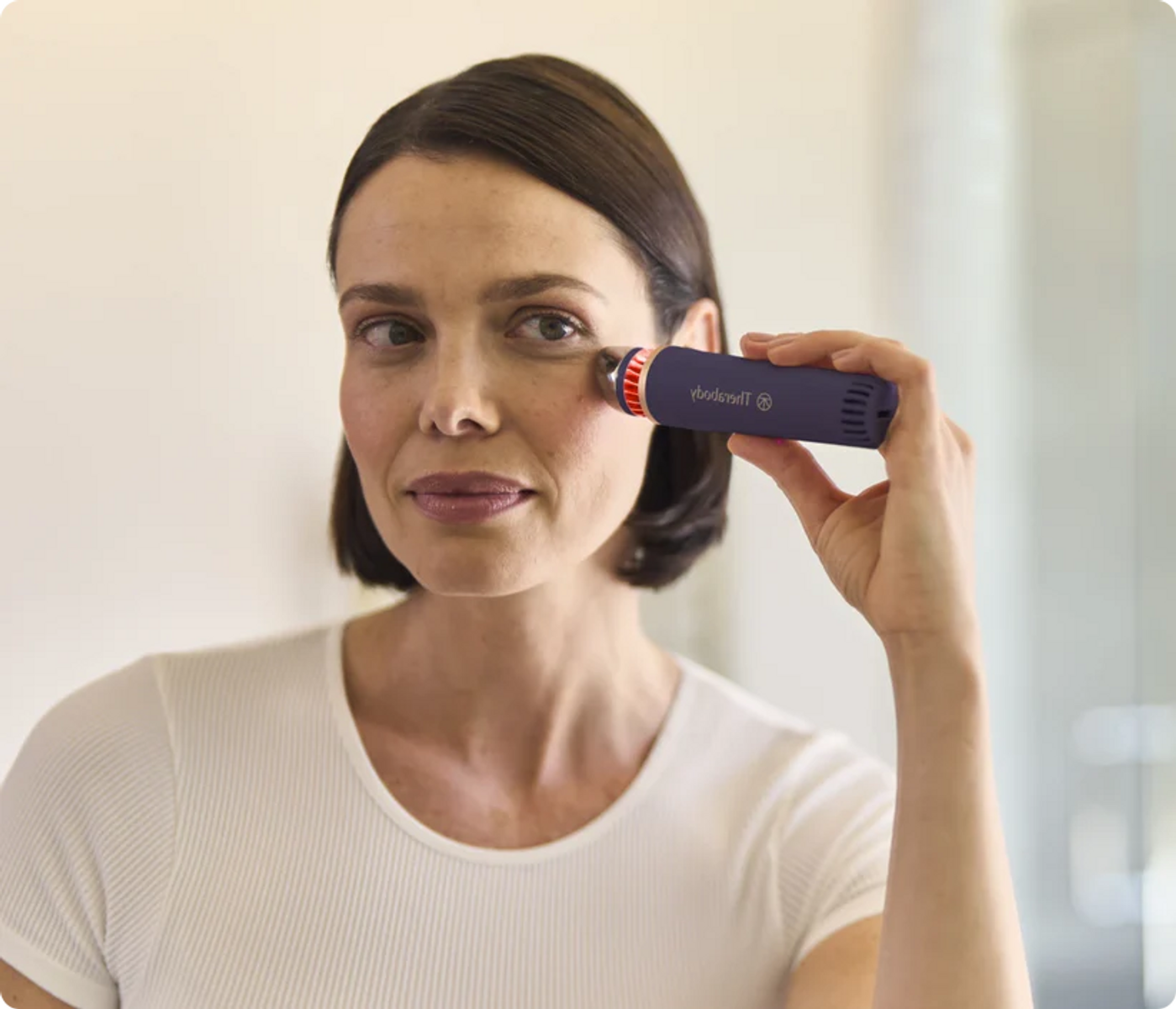 Una donna con capelli scuri usa un dispositivo per la cura della pelle blu.