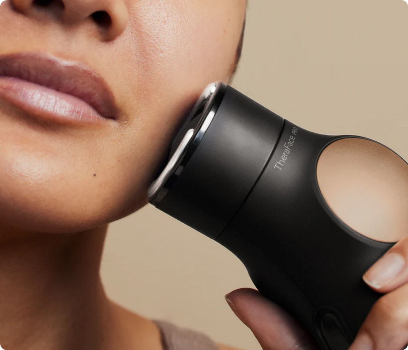 Una mano sostiene un dispositivo de masaje facial negro en la barbilla de una persona.