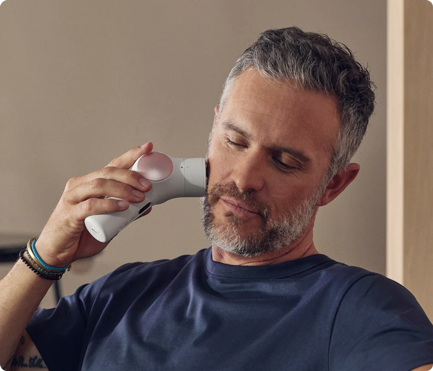 Hombre con barba usa un dispositivo de masaje facial blanco.
