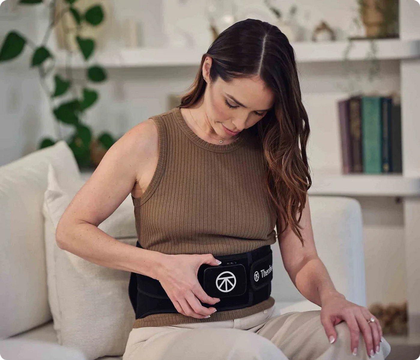 Mujer con cinturón abdominal negro sentada en un sofá, sujetándolo.