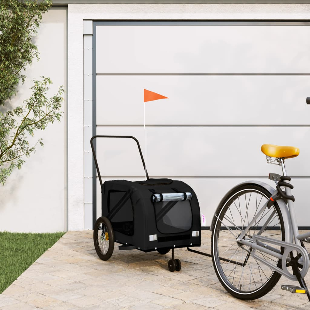Ein schwarzer Fahrradanhänger mit orangefarbener Flagge steht neben einem Fahrrad.