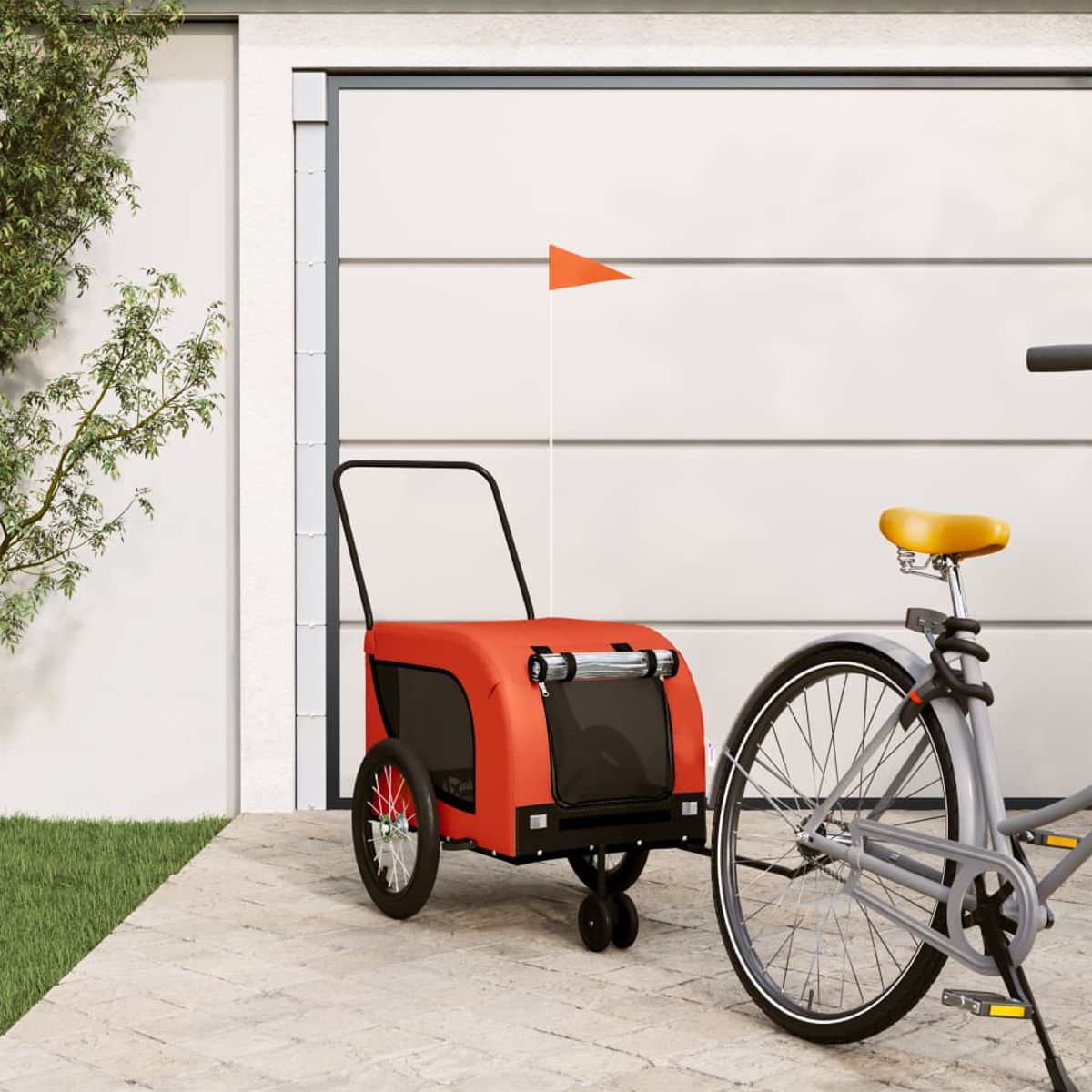 Ein roter Fahrradanhänger mit orangem Wimpel neben einem grauen Fahrrad.