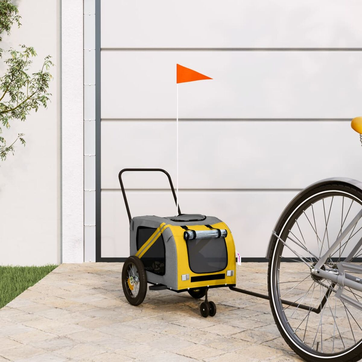 Ein gelber und grauer Kinderwagen mit orangenem Fähnchen vor einem Garagentor.
