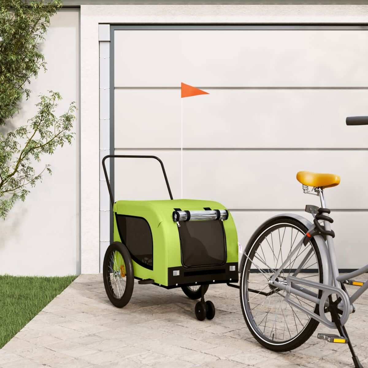 Ein grüner Fahrradanhänger mit orangefarbener Fahne neben einem Fahrrad vor einer Garage.