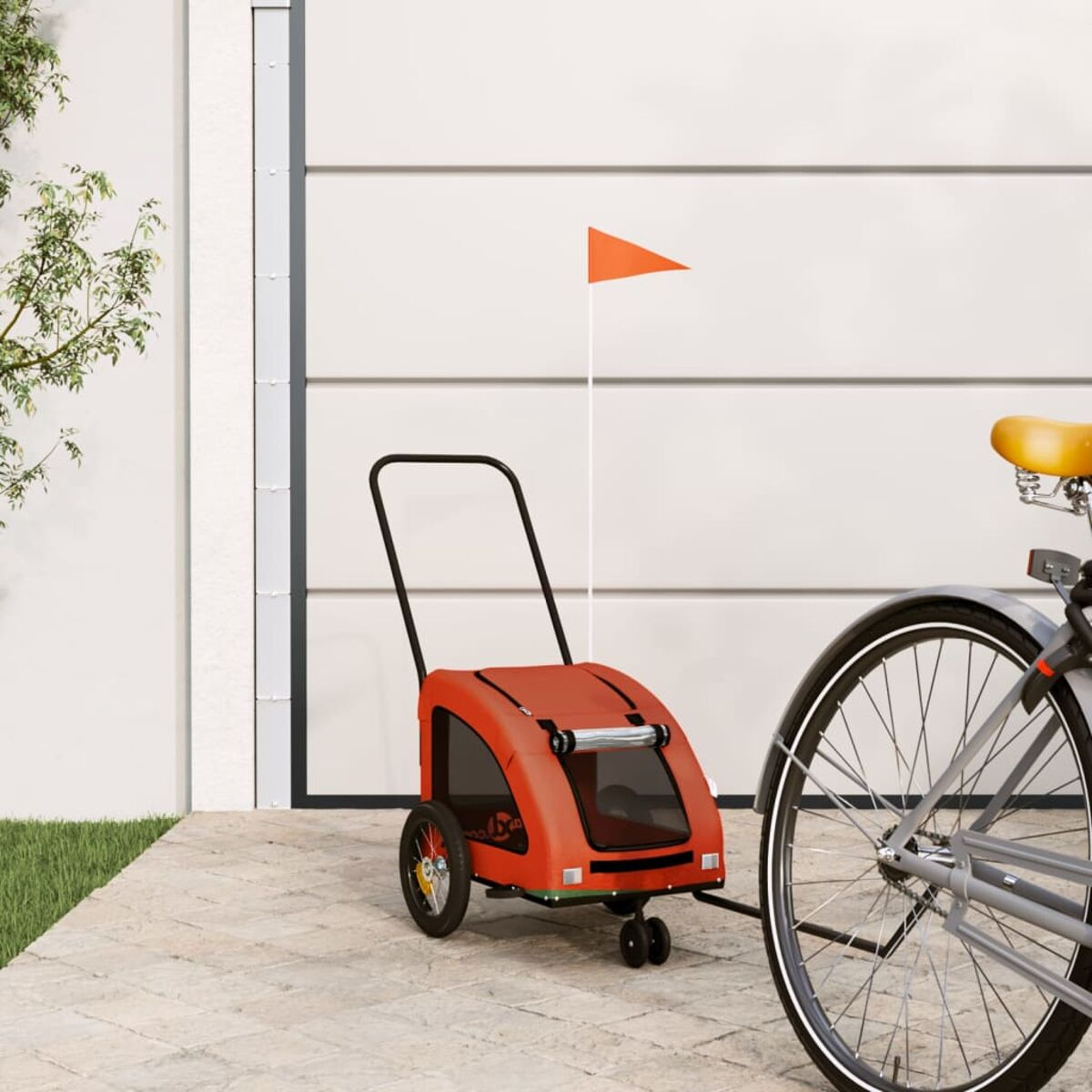 Ein orangefarner Fahrradanhänger mit Flagge steht neben einem Fahrrad vor einem Garagentor.