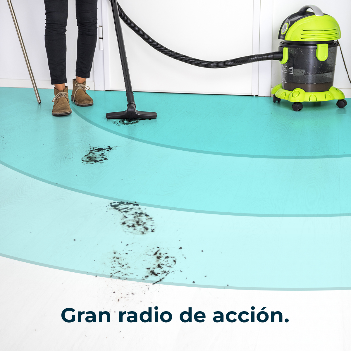 Osoba odkurza brud na jasnoniebieskiej podłodze zielonym odkurzaczem.