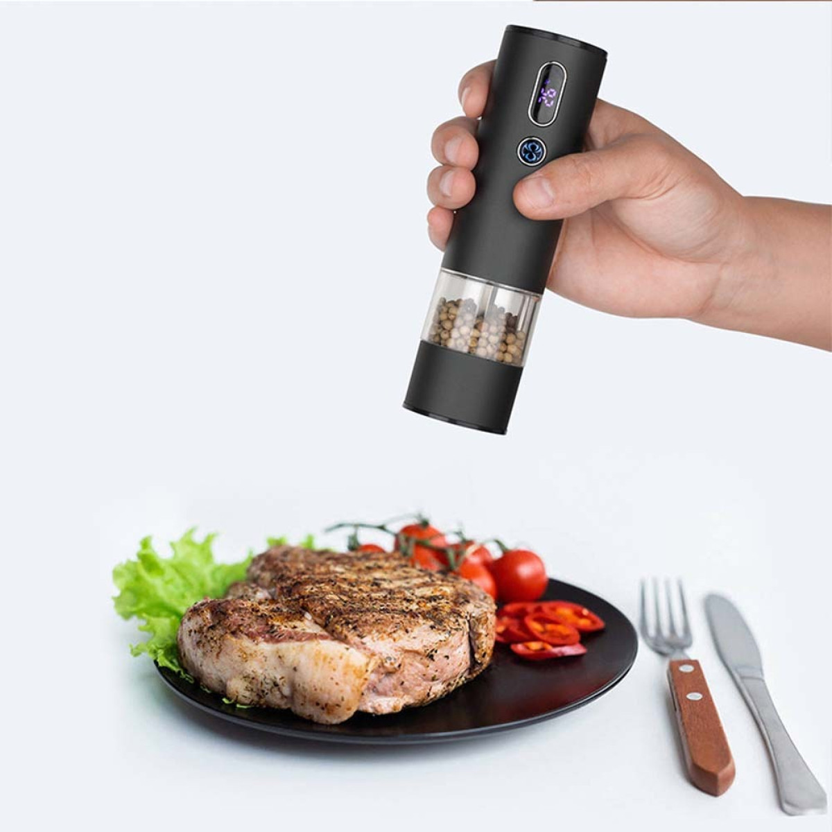 Ein Mann hält eine elektrische Pfeffermühle über ein Steak mit Beilagen.