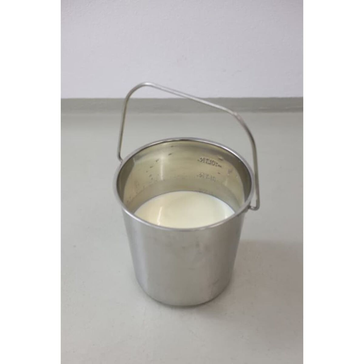 Ein Metallbecher mit Henkel, gefüllt mit weißer Flüssigkeit.