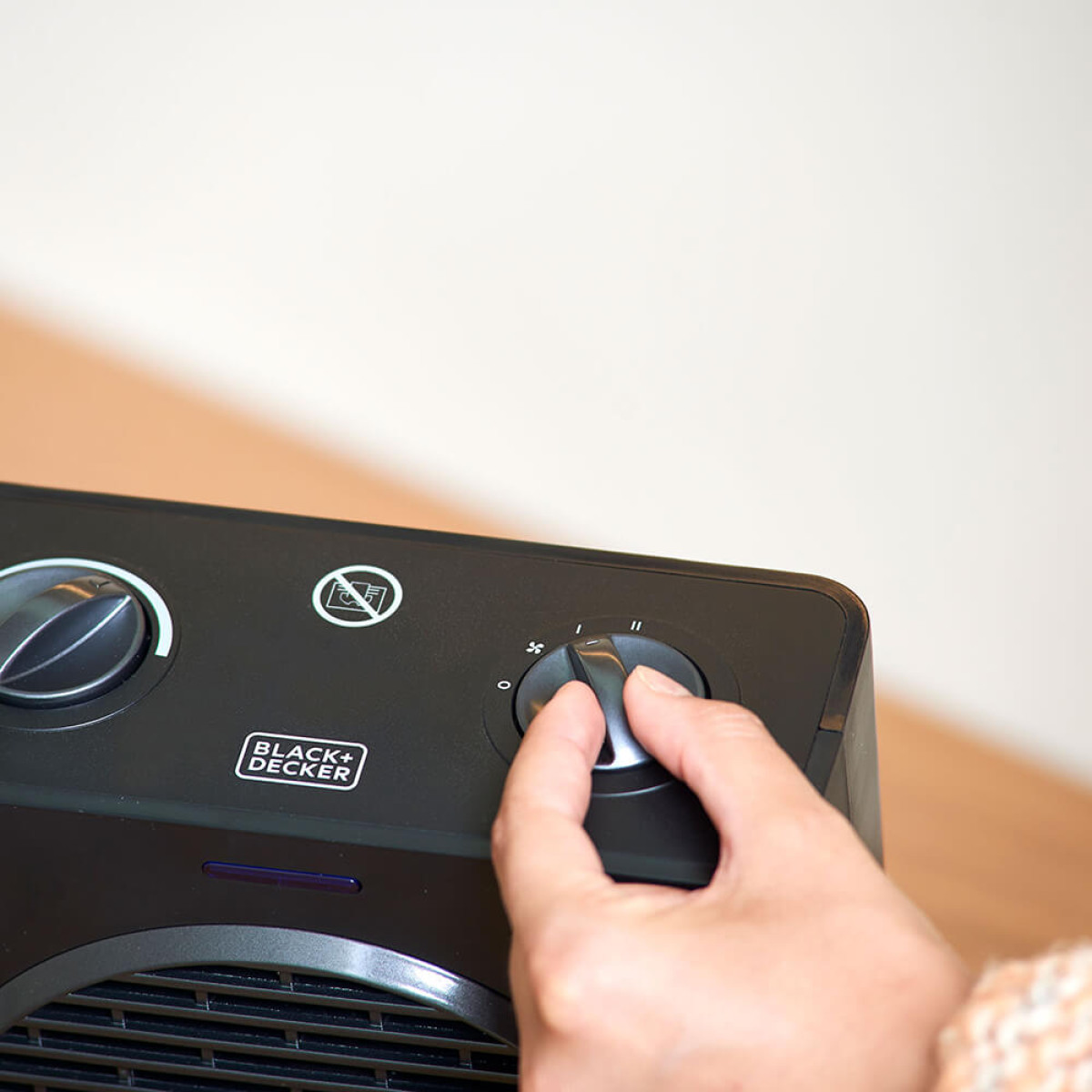 Ręka przekręca pokrętło w czarnym grzejniku z symbolem wentylatora.