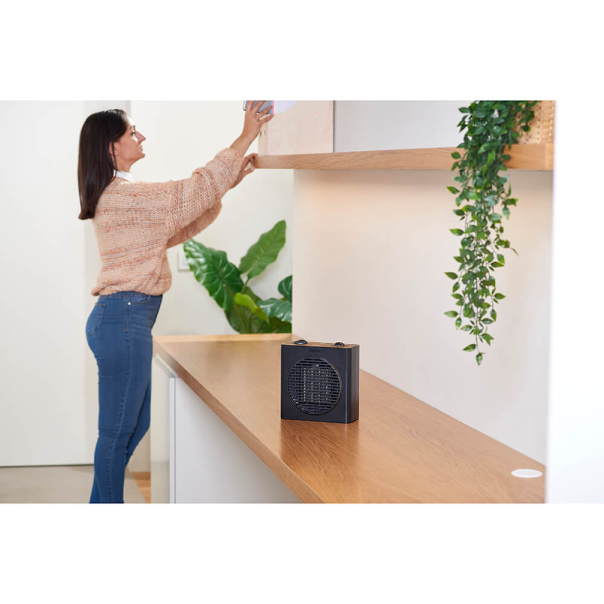 Kobieta kładzie przedmiot na półce. Czarny grzejnik na drewnianym blacie.