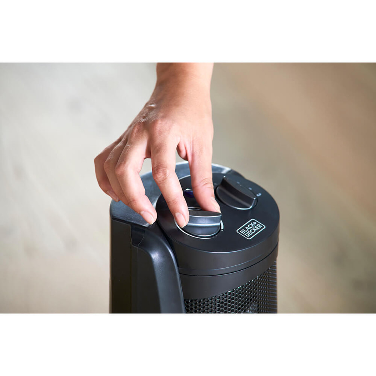 Dłoń obraca pokrętło na czarnym przenośnym grzejniku.