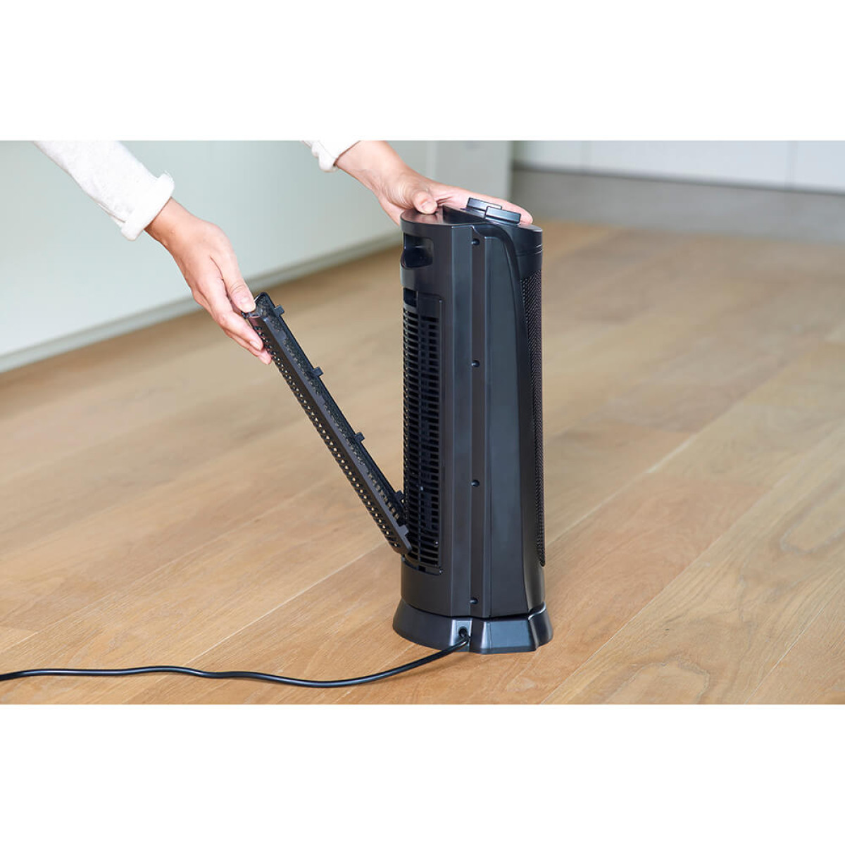 Osoba wyjmuje czarny filtr z wentylatora wieżowego na drewnianej podłodze.