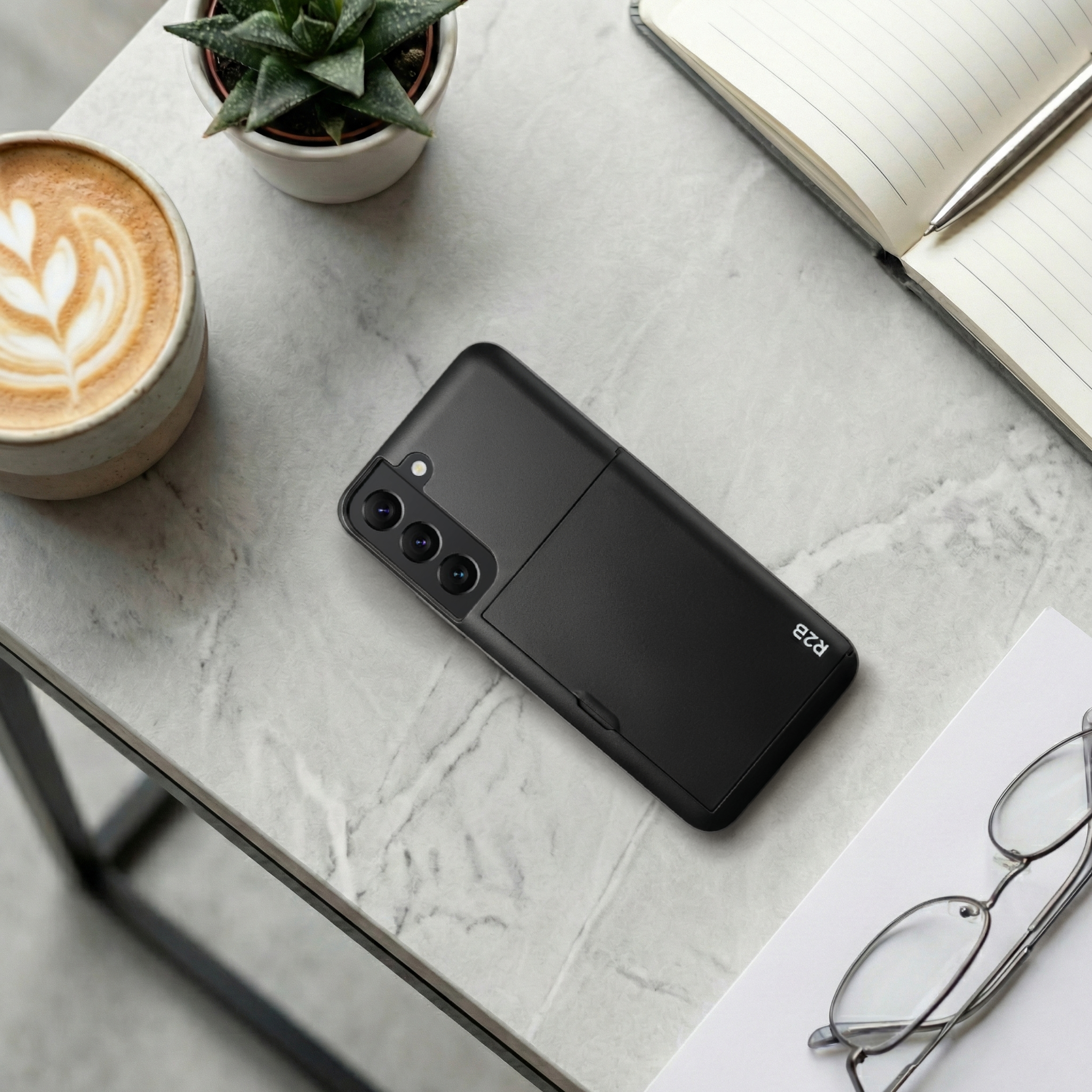 Smartphone noir sur table marbre avec café et plante.
