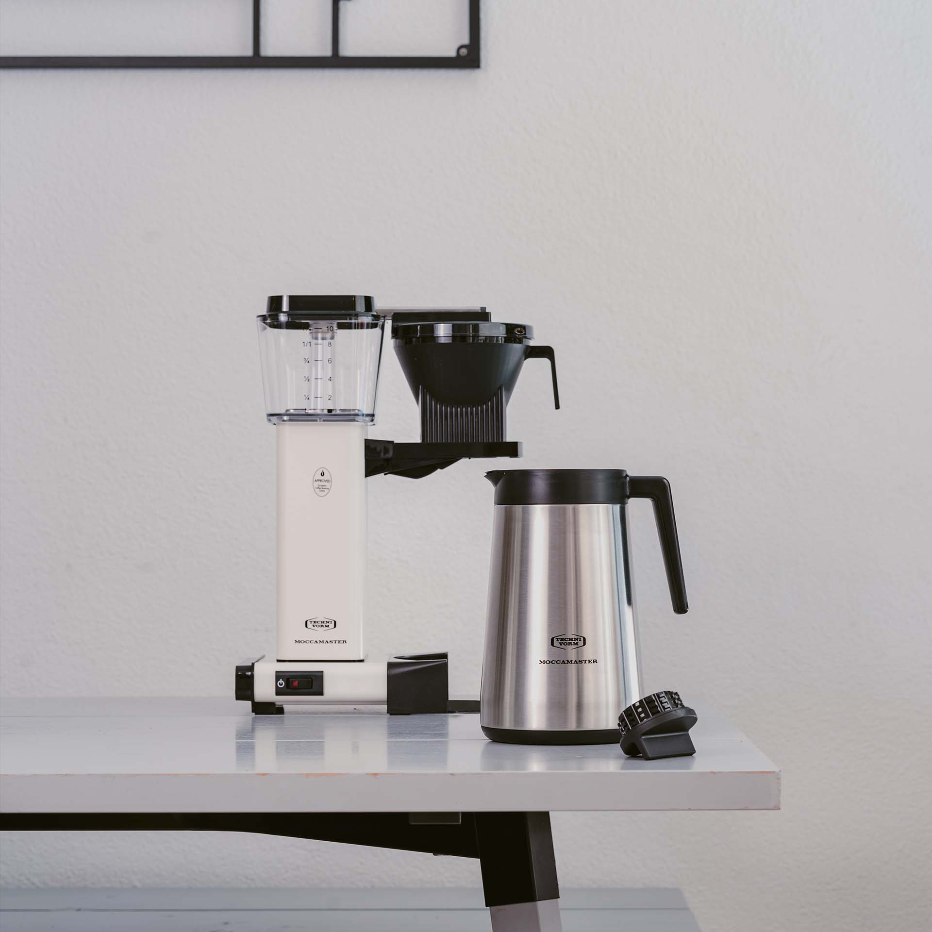 Una macchina da caffè bianca con caraffa argentata è sul tavolo.