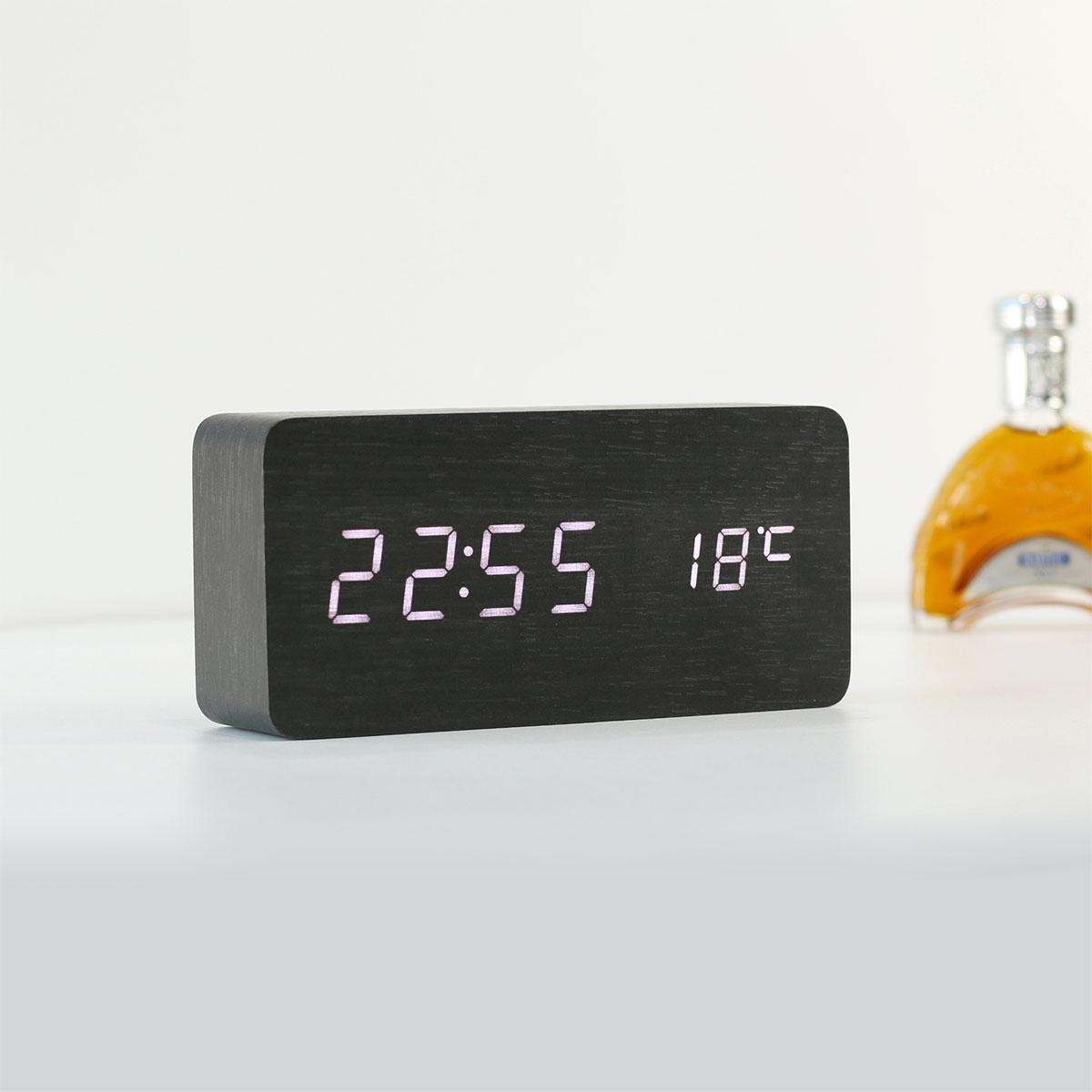 Czarny zegar cyfrowy pokazuje 22:55 i 18°C. Obok stoi butelka.
