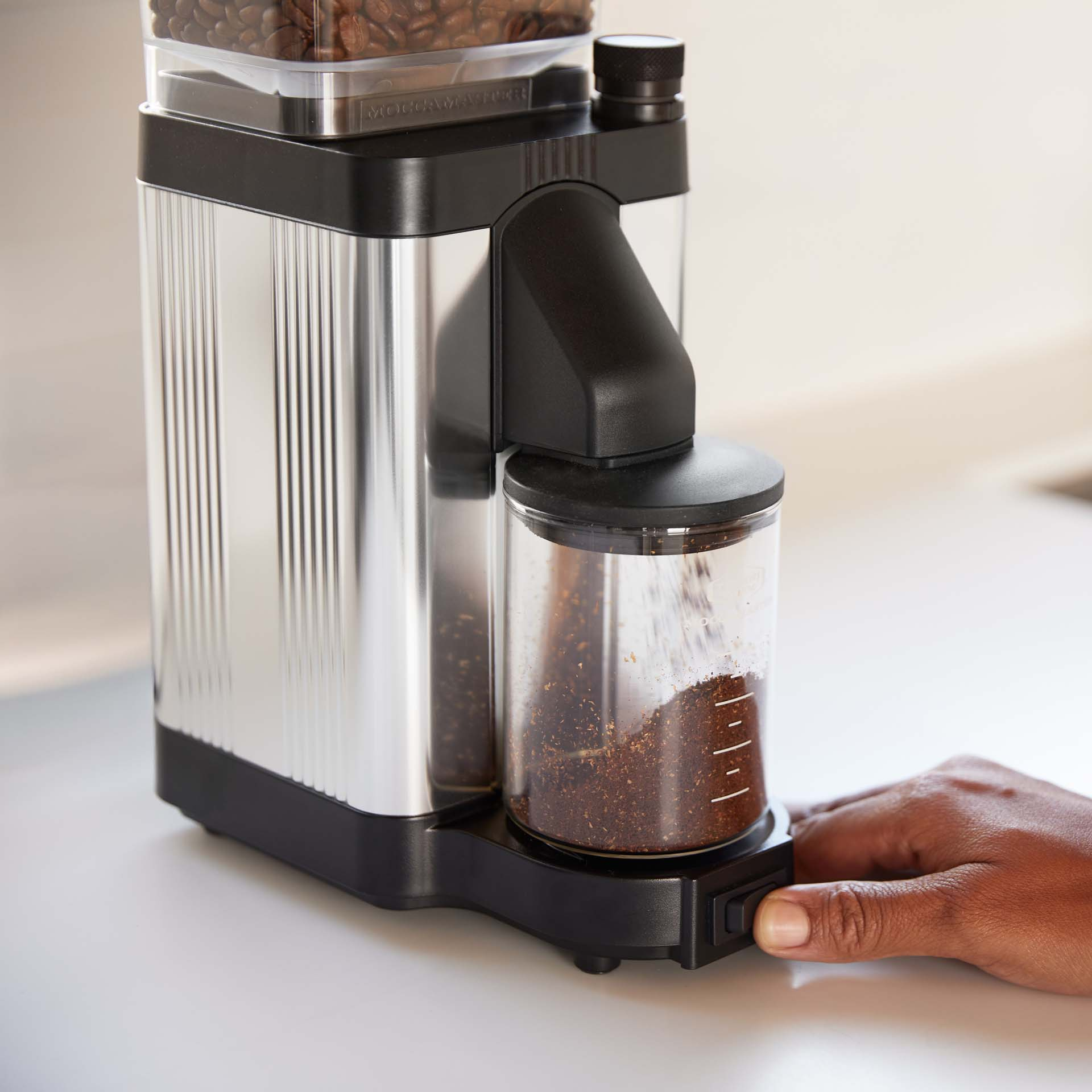 Coffee grinder with silver body, black lid, and glass container with ground coffee.