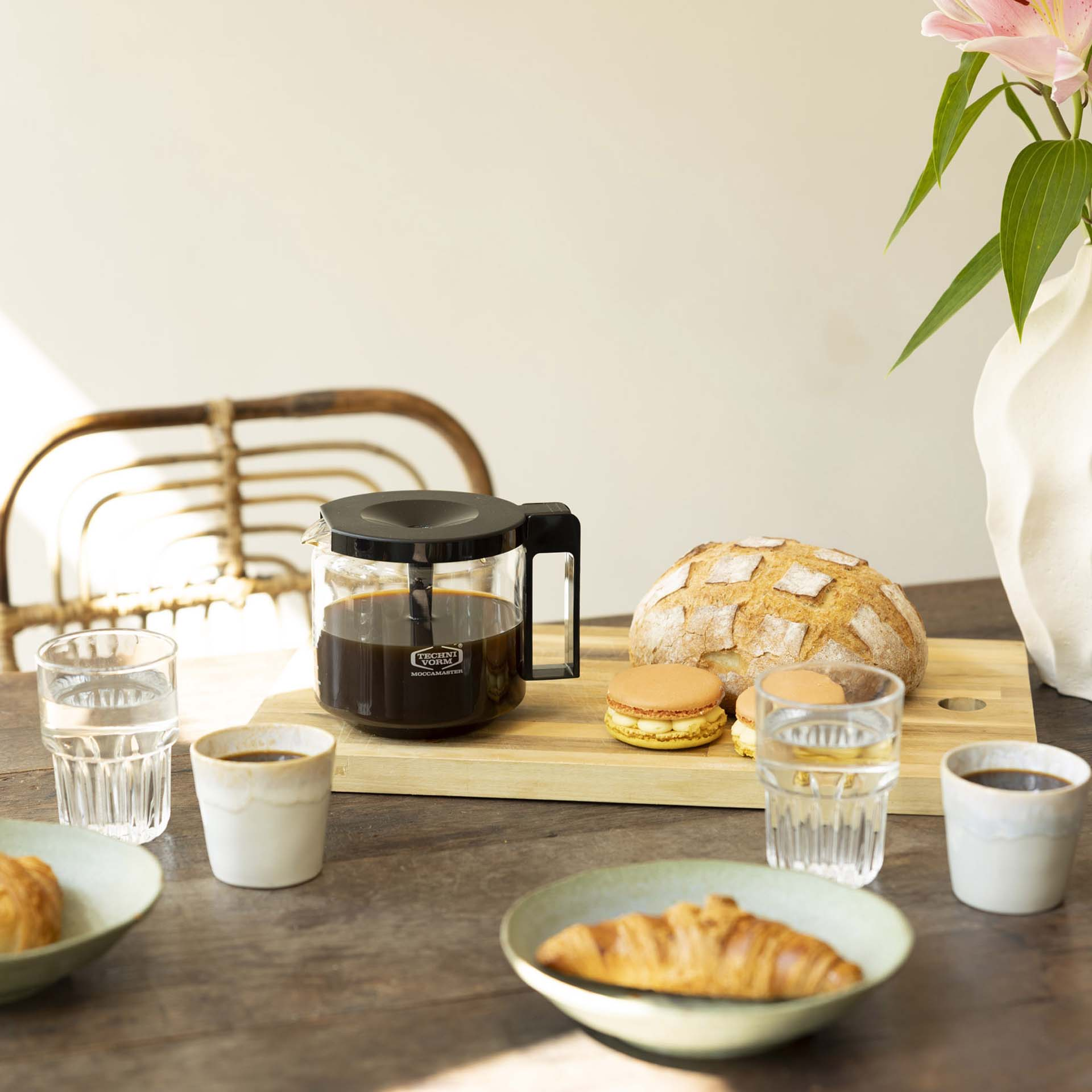 Carafe à café, pain, macarons et pâtisseries sur une table en bois.
