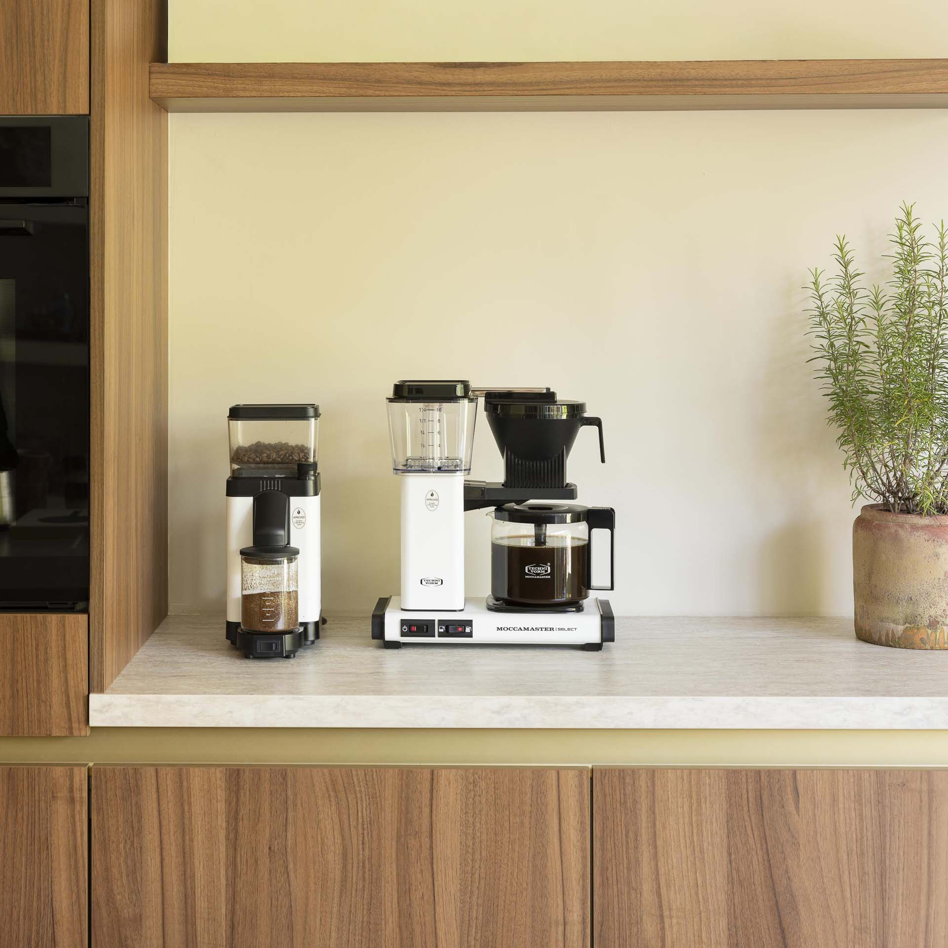 Eine weiße Kaffeemühle und eine Moccamaster Kaffeemaschine stehen auf einer Arbeitsplatte.