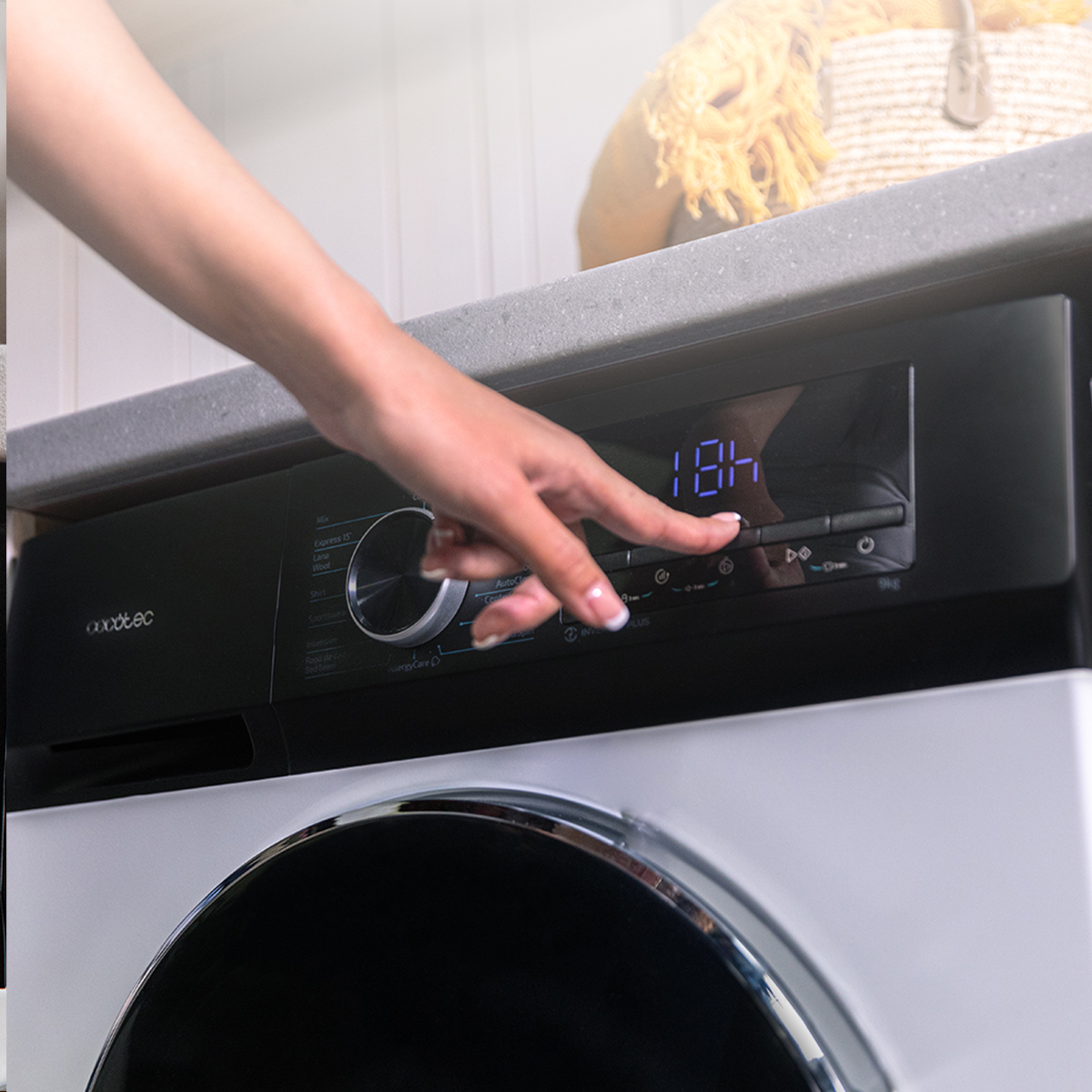 Una mano preme un pulsante su una lavatrice con display digitale.