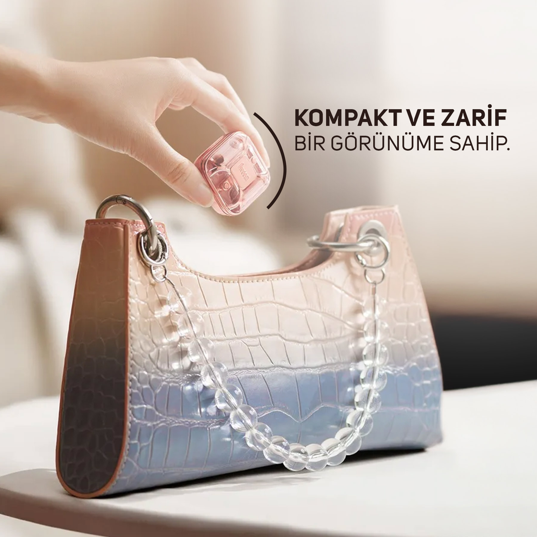 Bir el, timsah derisi desenli bir el çantasının üzerinde küçük pembe kare bir kutu tutuyor.