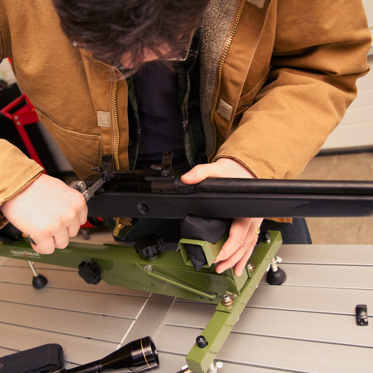 Una persona trabaja en un rifle, sujeto por un soporte verde. Se ve una multiherramienta.