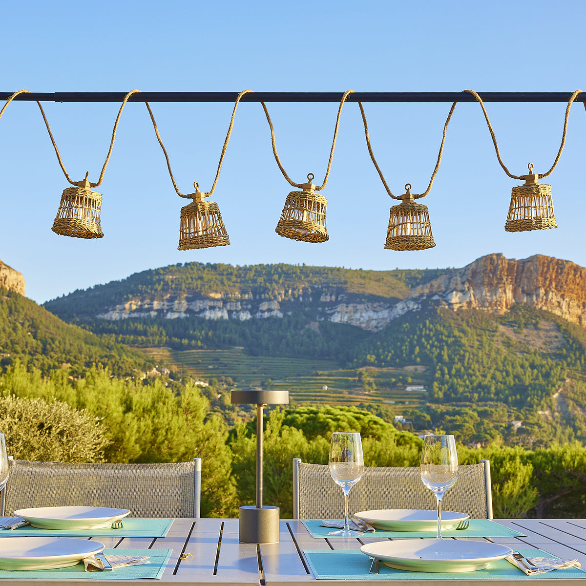 Geflochtene Laternen hängen über einem für das Abendessen gedeckten Tisch mit Bergblick.
