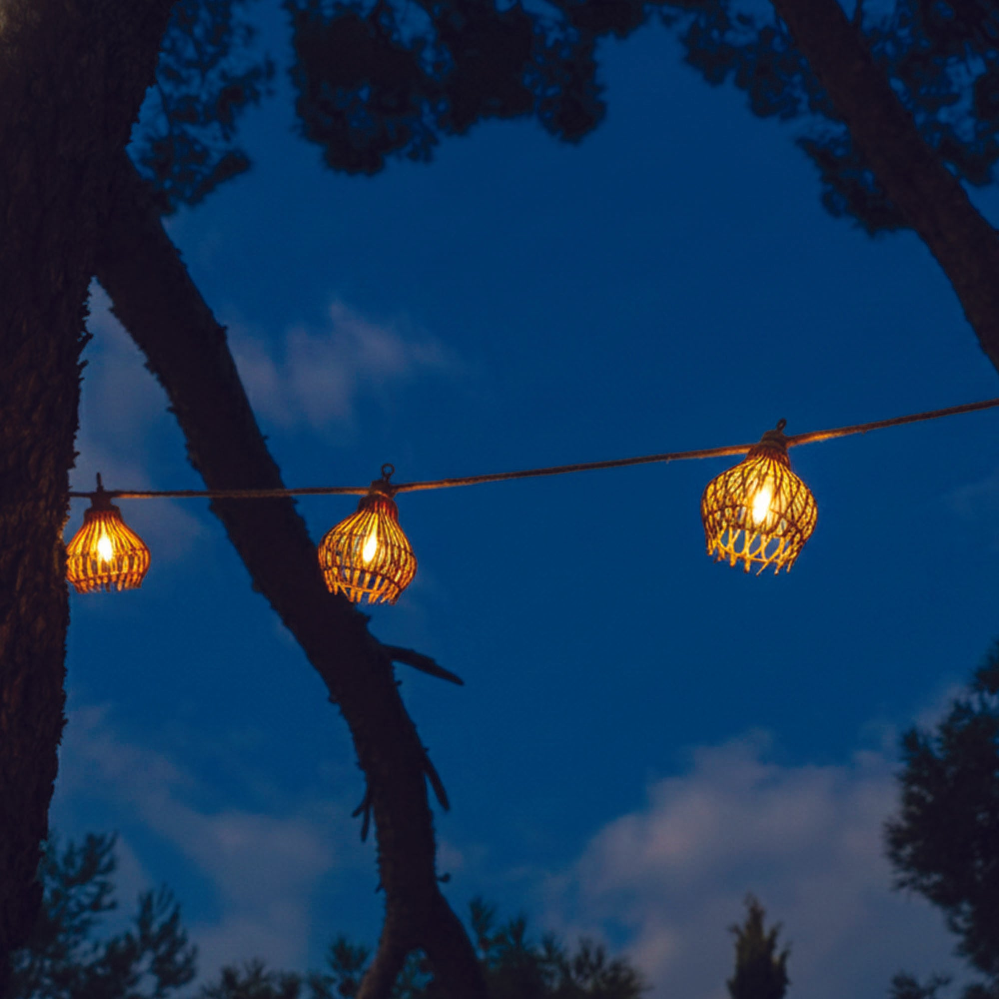 Drei Lichterketten mit Korbförmigen Lampen hängen vor dem Nachthimmel.