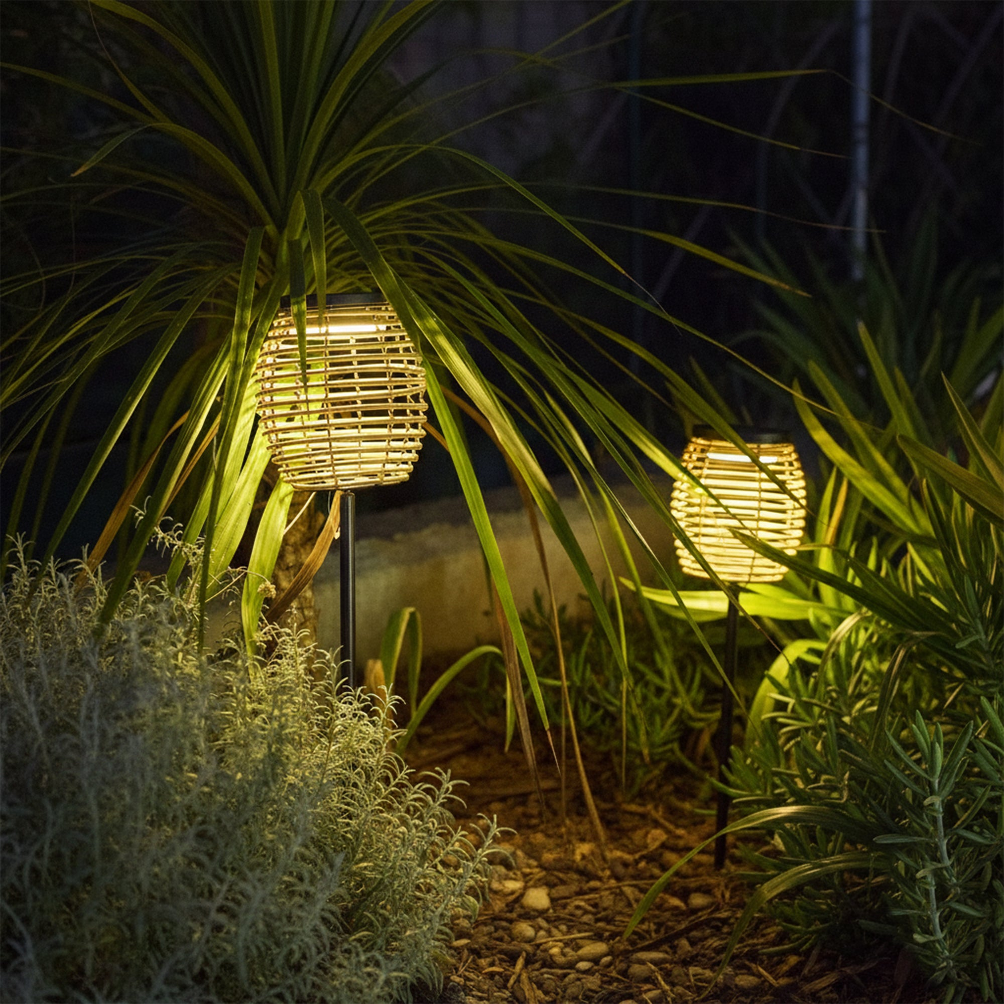 Zwei geflochtene Solarlampen beleuchten einen dunklen Garten mit üppigem Grün.