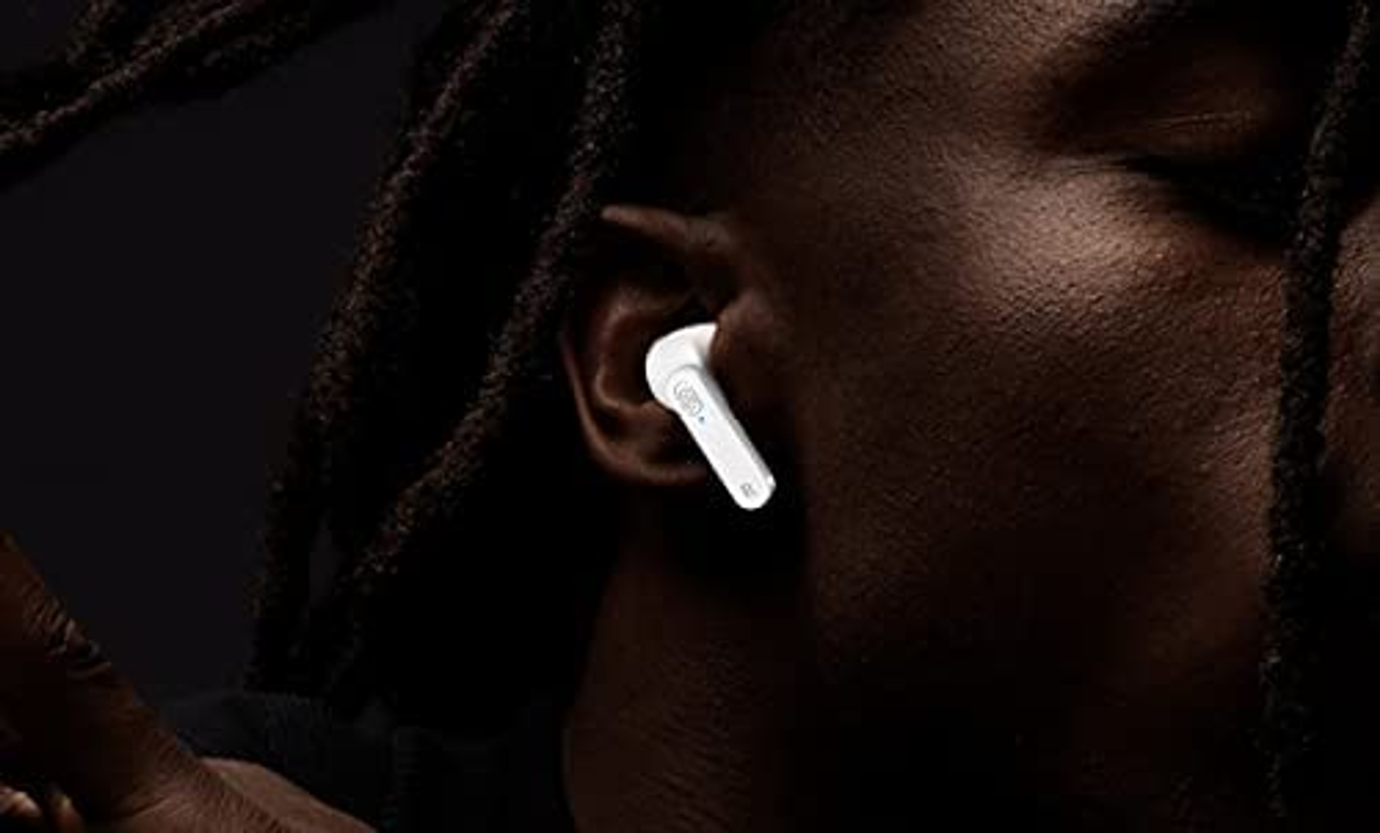 Biała słuchawka w ciemnym uchu, z ciemnymi włosami w tle.
