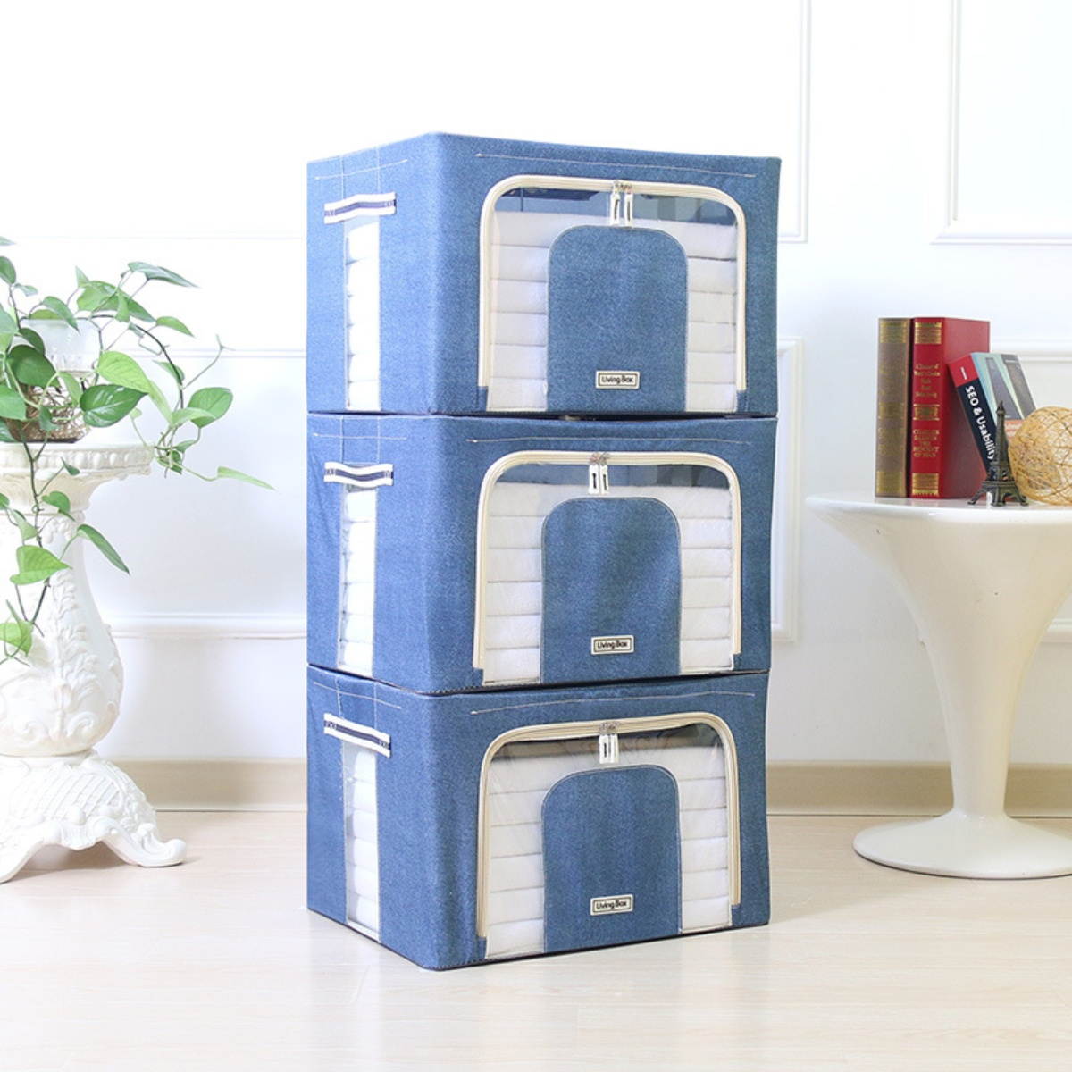 Drei blaue Stoffboxen mit Fenstern, gestapelt. Links eine Pflanze.