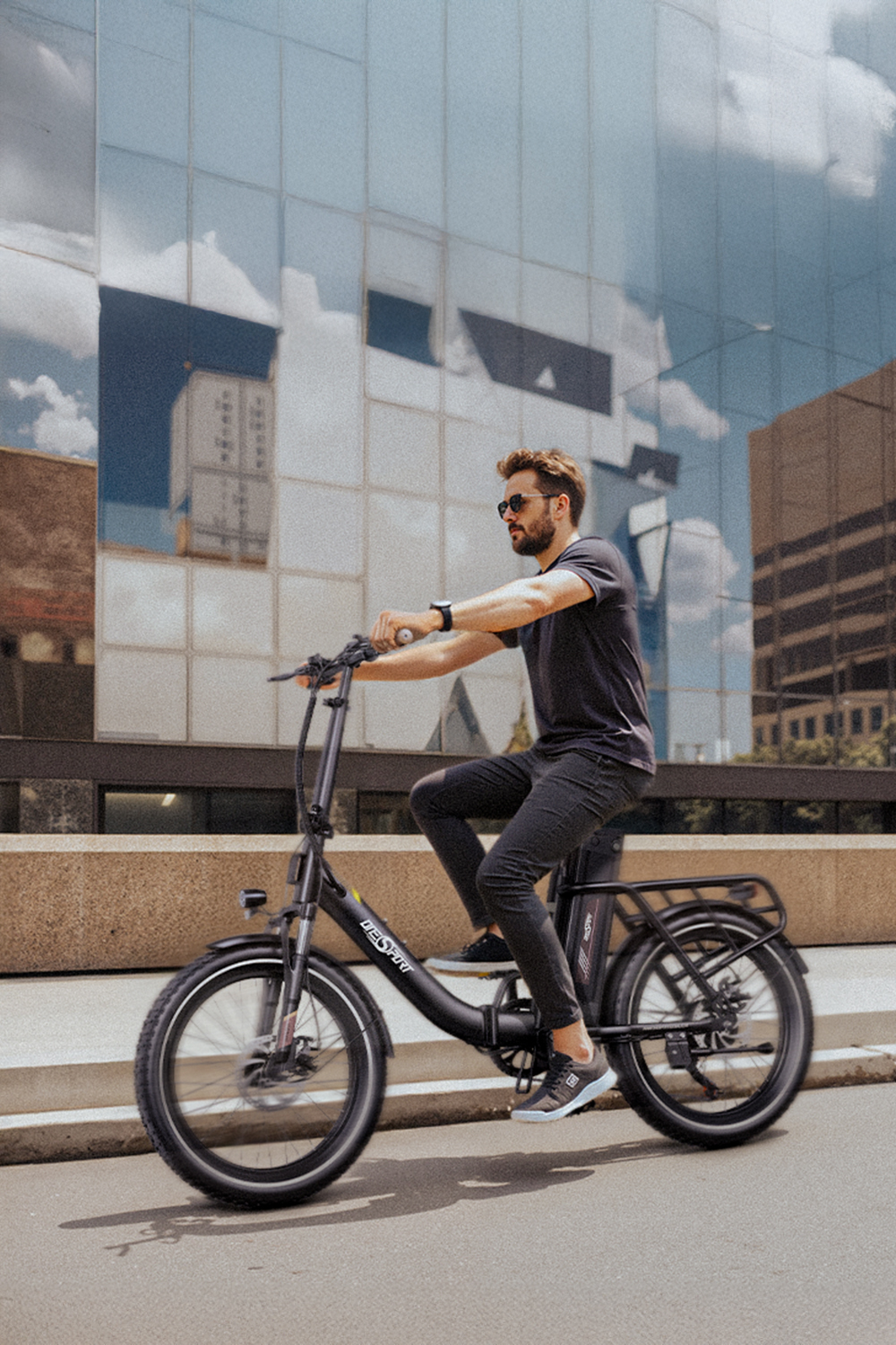Ein Mann in dunkler Kleidung fährt ein schwarzes E-Bike vor einem modernen Gebäude.