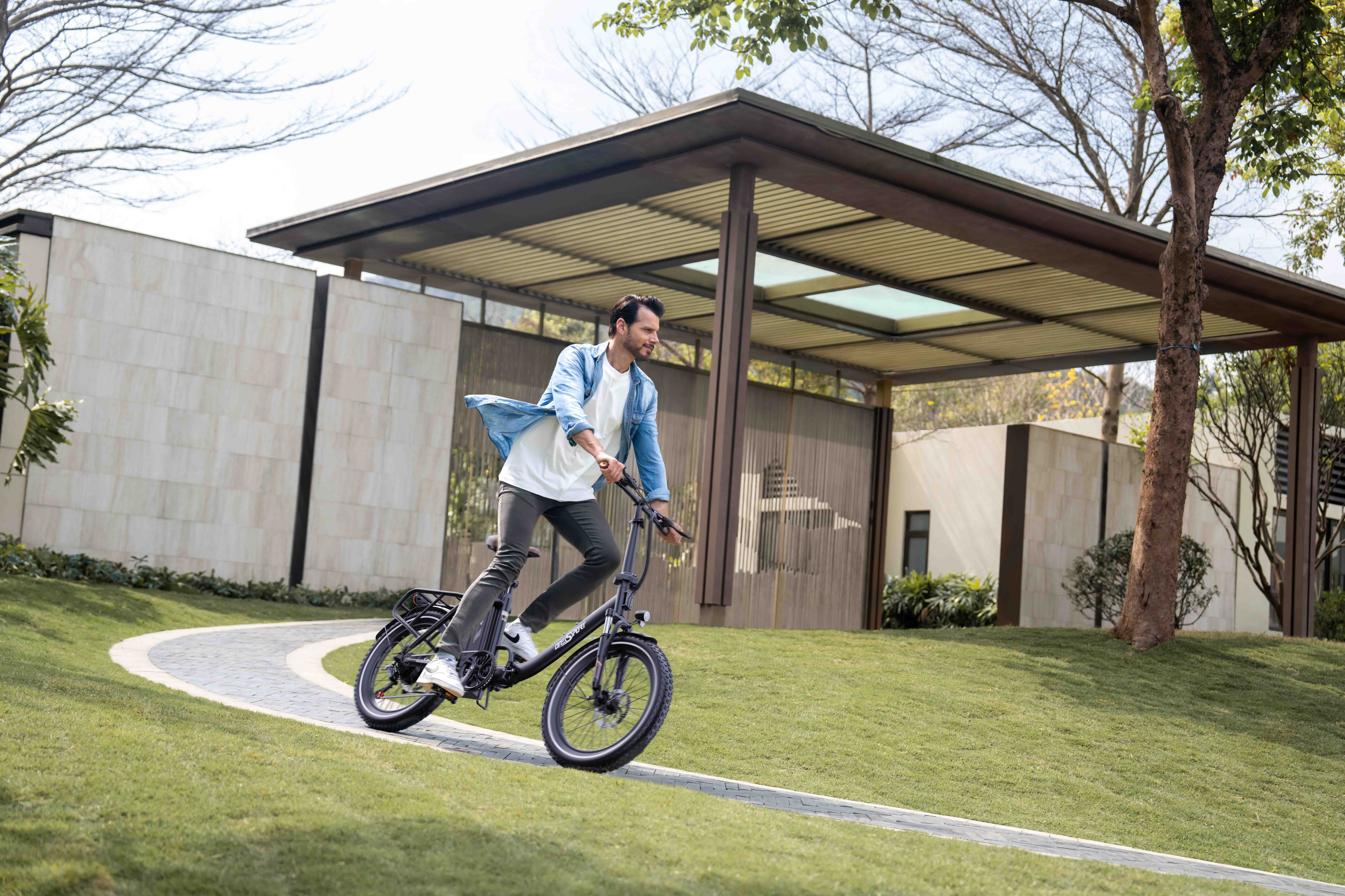 Ein Mann fährt auf einem schwarzen E-Bike auf einem gepflasterten Weg durch einen gepflegten Garten.