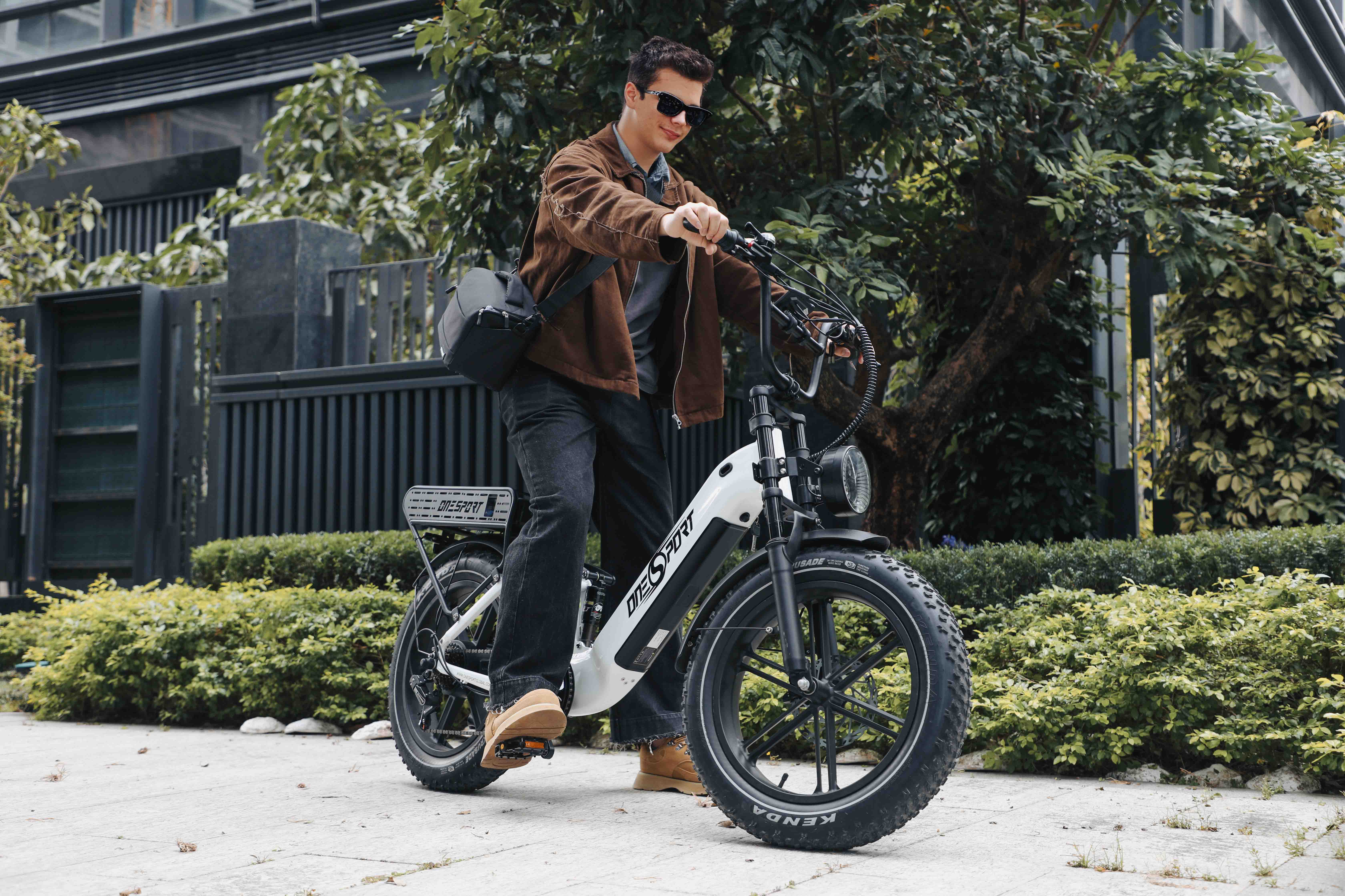 Ein Mann fährt ein weißes E-Bike auf einem Gehweg, umgeben von Bäumen und Zäunen.