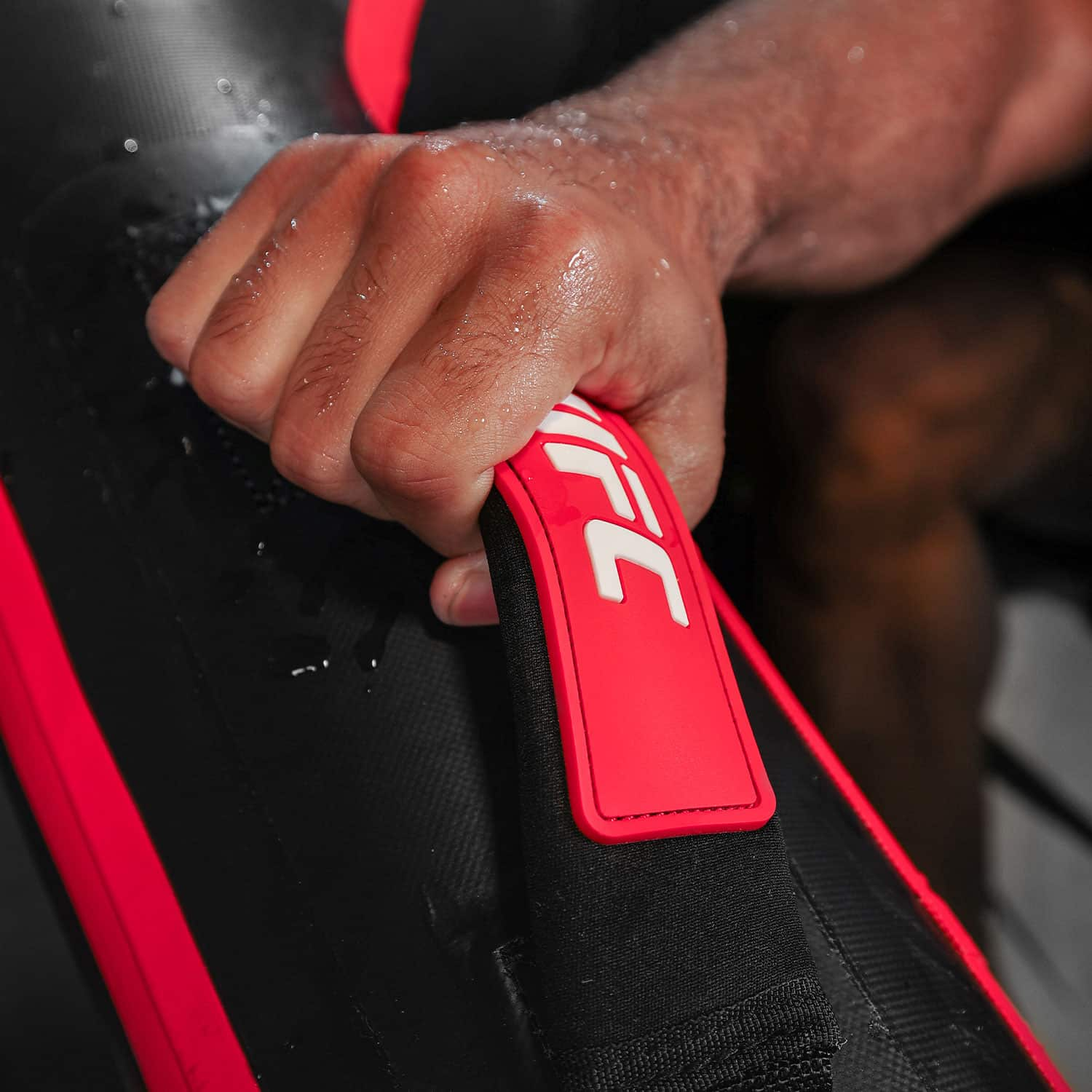 Una mano agarra un asa roja de UFC en un equipo de entrenamiento mojado.