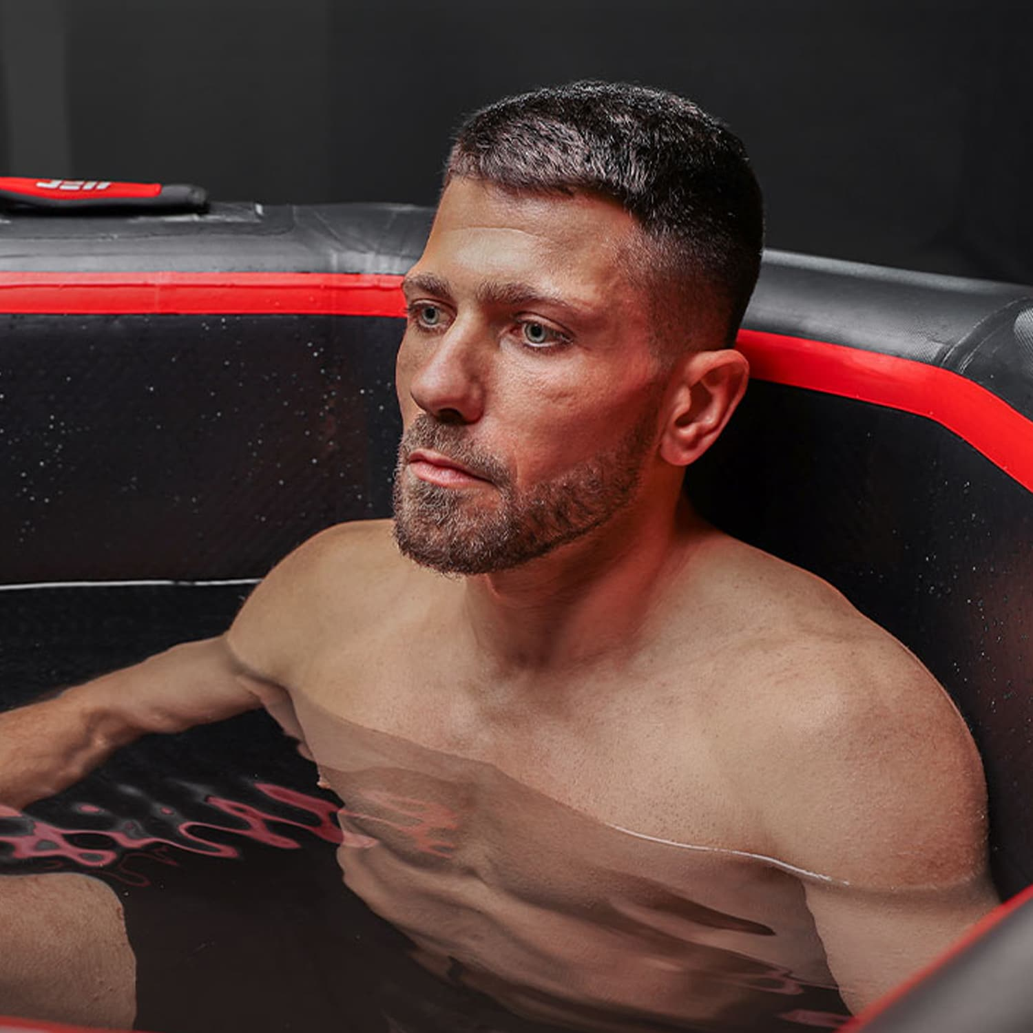 Un hombre se sienta en una tina inflable negra y roja con agua.
