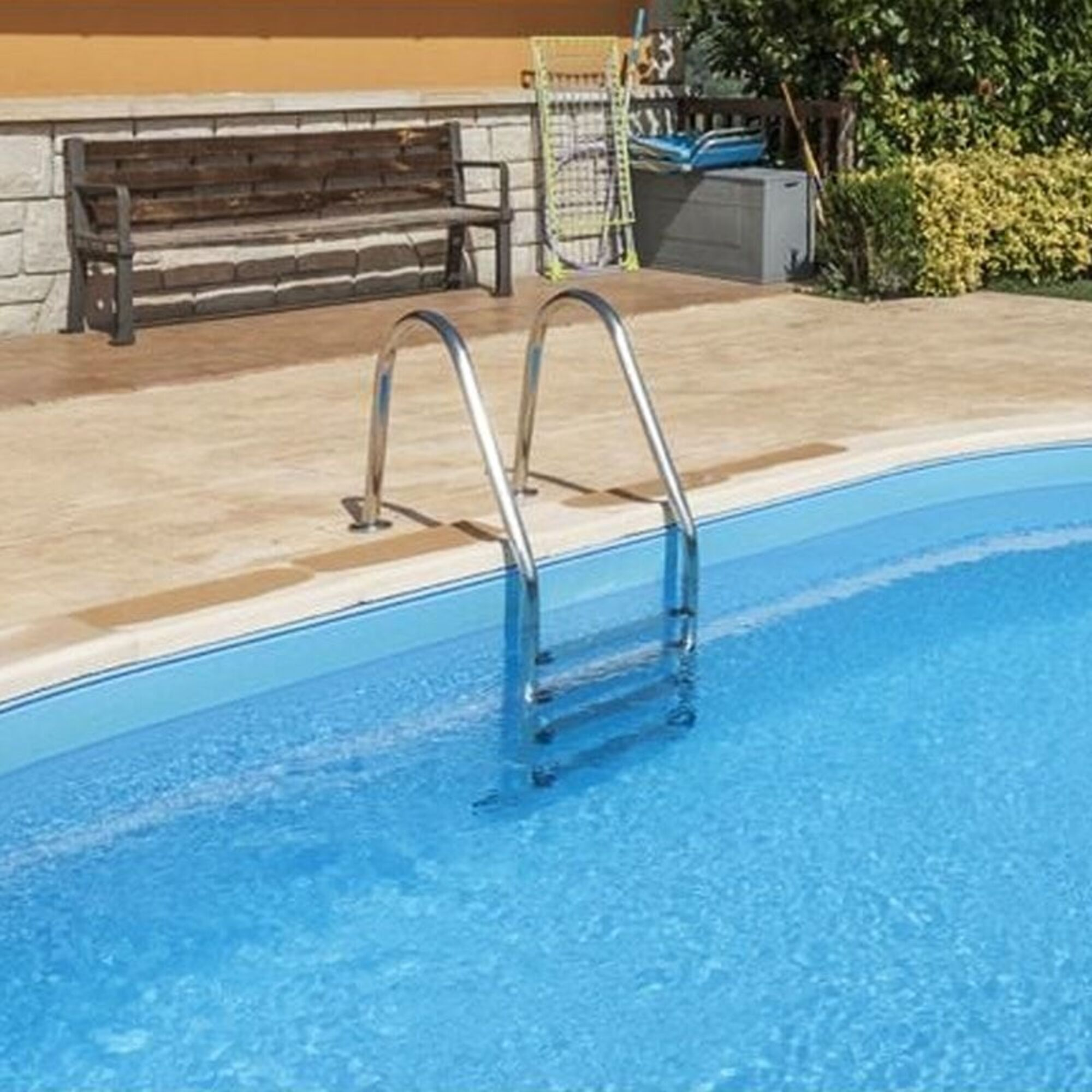 Una piscina con escalera, al lado un banco de madera, tendedero y caja de almacenamiento.