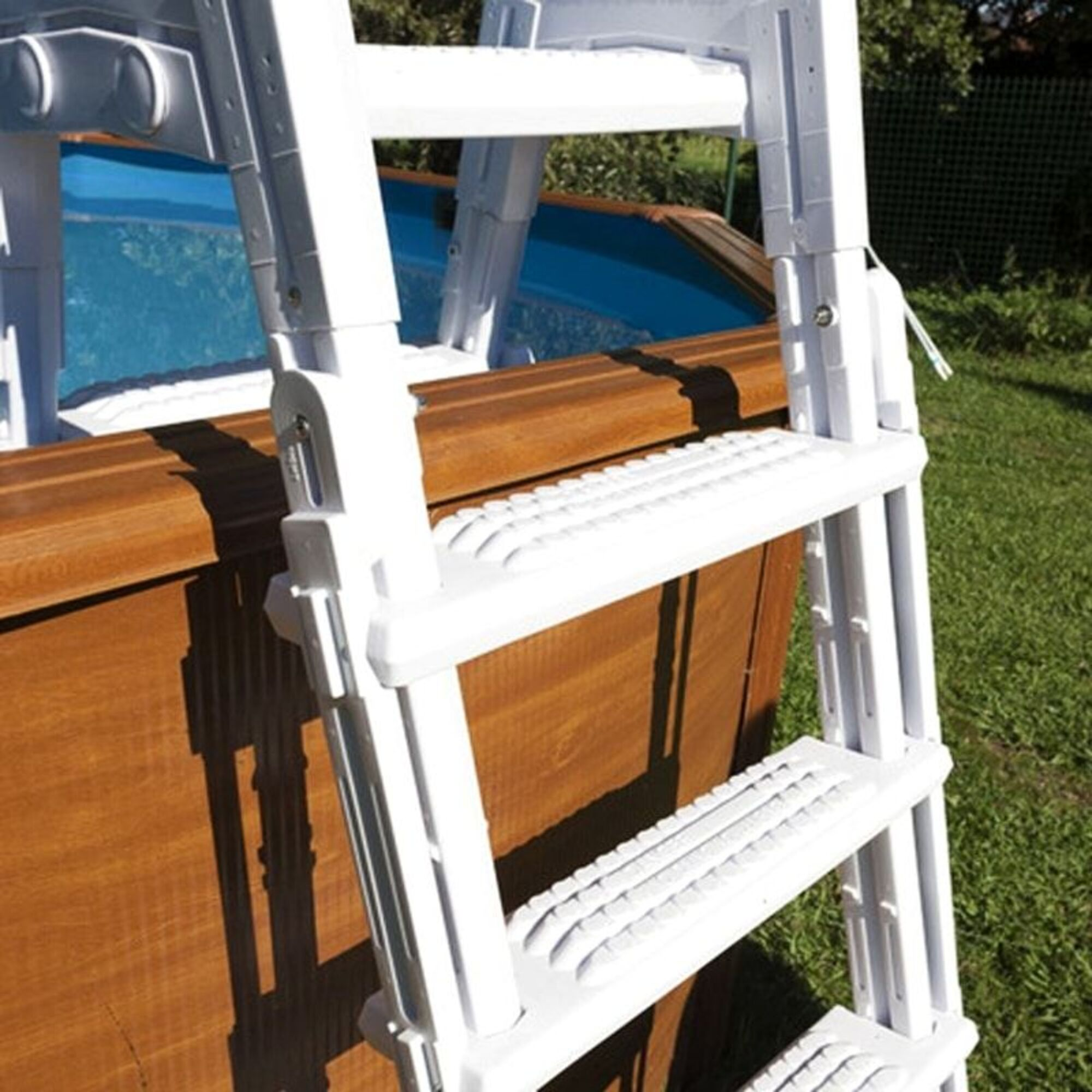 Escalera de piscina blanca sobre borde de piscina de madera con agua azul.