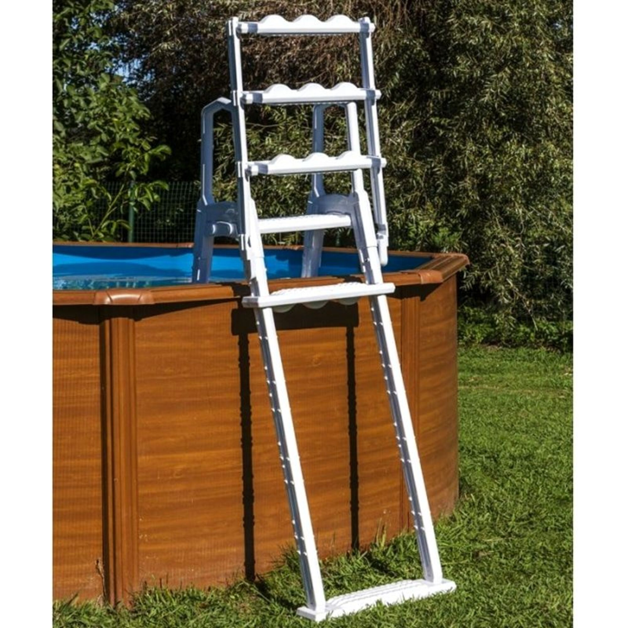 Una escalera blanca junto a una piscina de madera con agua azul.