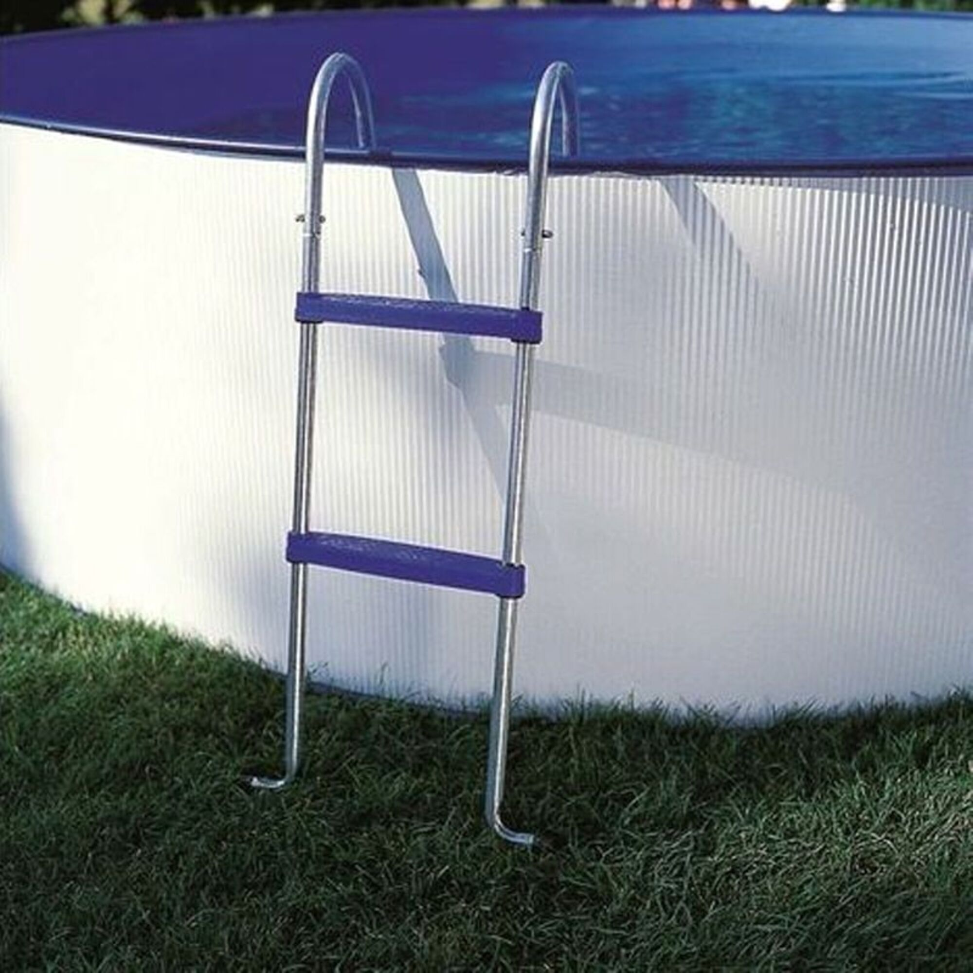 Una escalera de piscina plateada con peldaños azules está sobre césped junto a una piscina blanca.