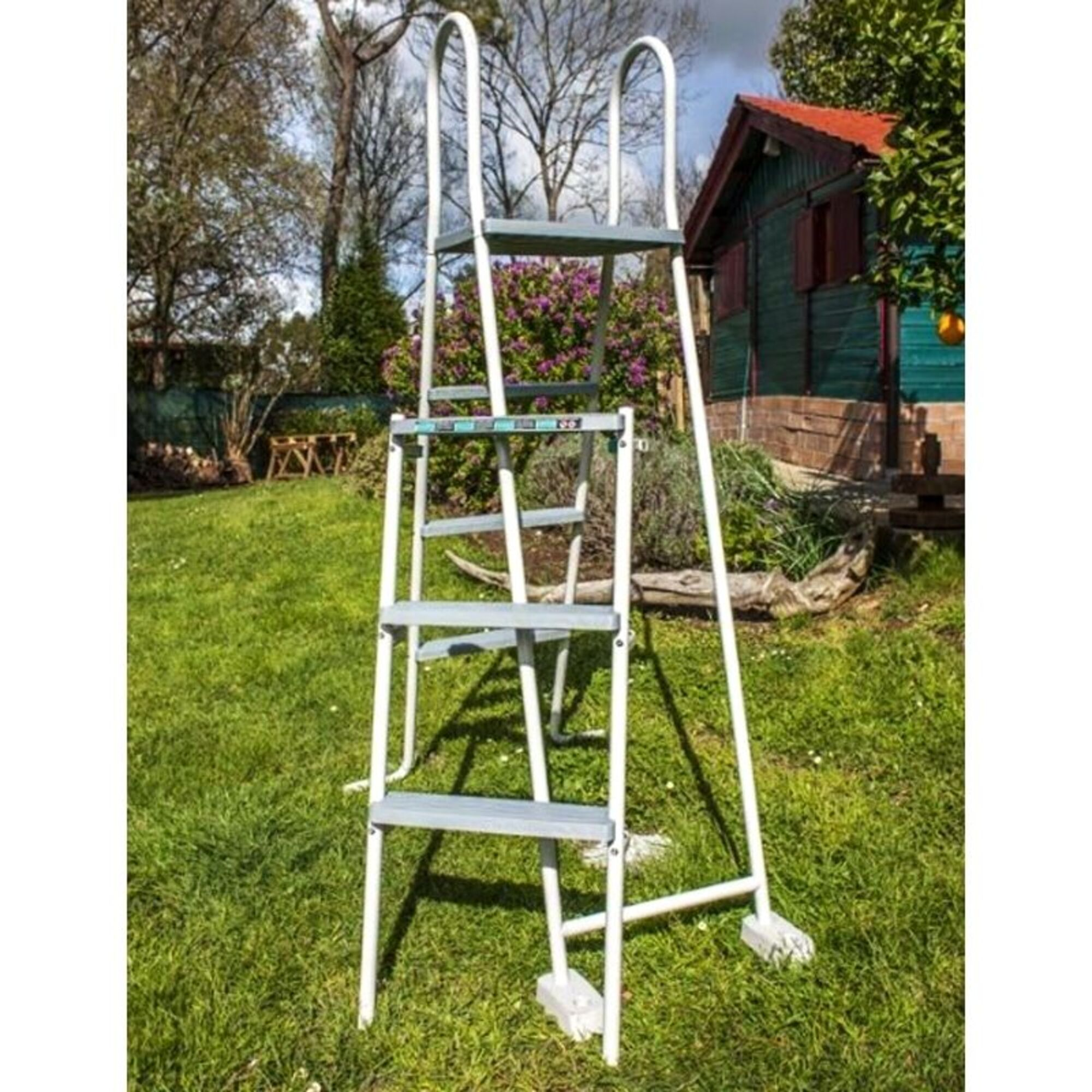 Una escalera blanca con peldaños grises está sobre césped verde frente a un cobertizo de madera.