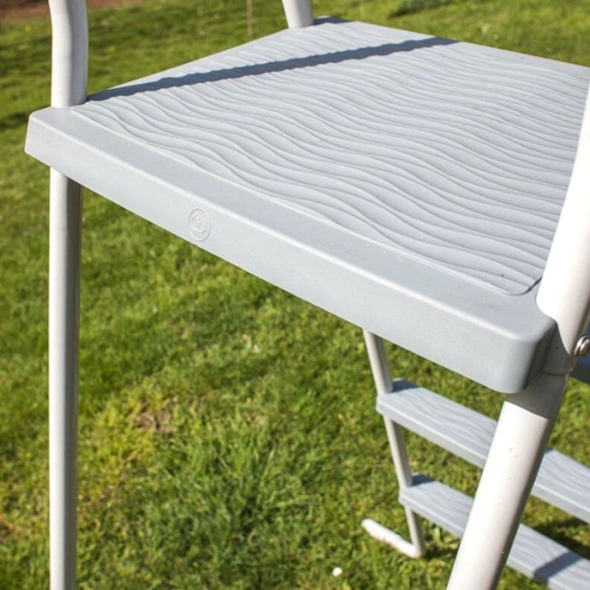 Una escalera gris con peldaños de patrón ondulado sobre hierba verde.