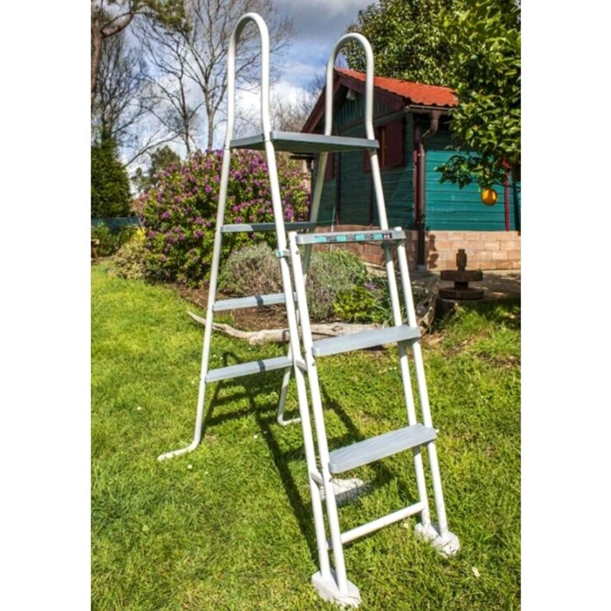 Una escalera blanca con escalones grises se alza sobre un césped delante de un cobertizo verde.