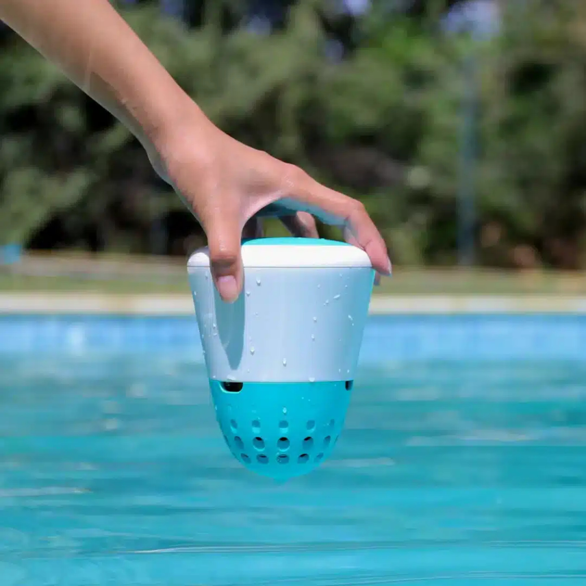 Una mano sostiene un dispositivo blanco y azul sobre el agua de una piscina.