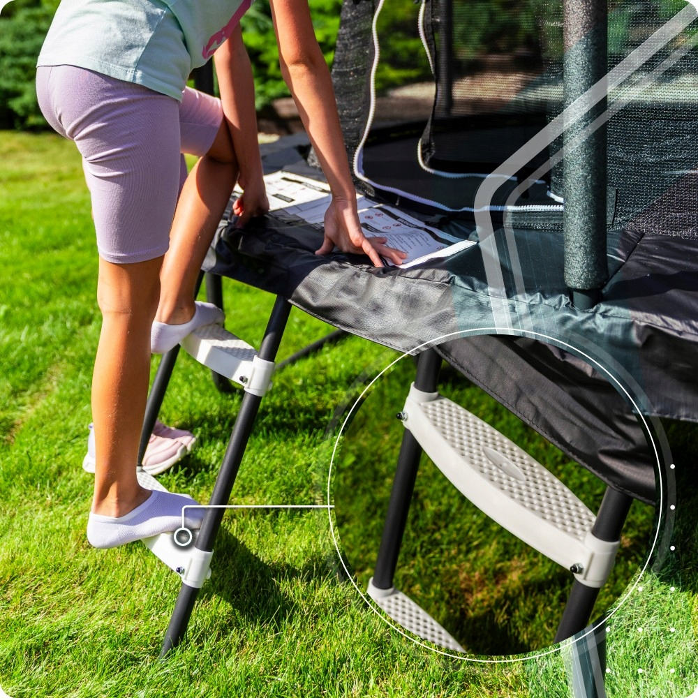 Dziewczynka wspina się po drabinie trampoliny z instrukcją. Trawa w tle.