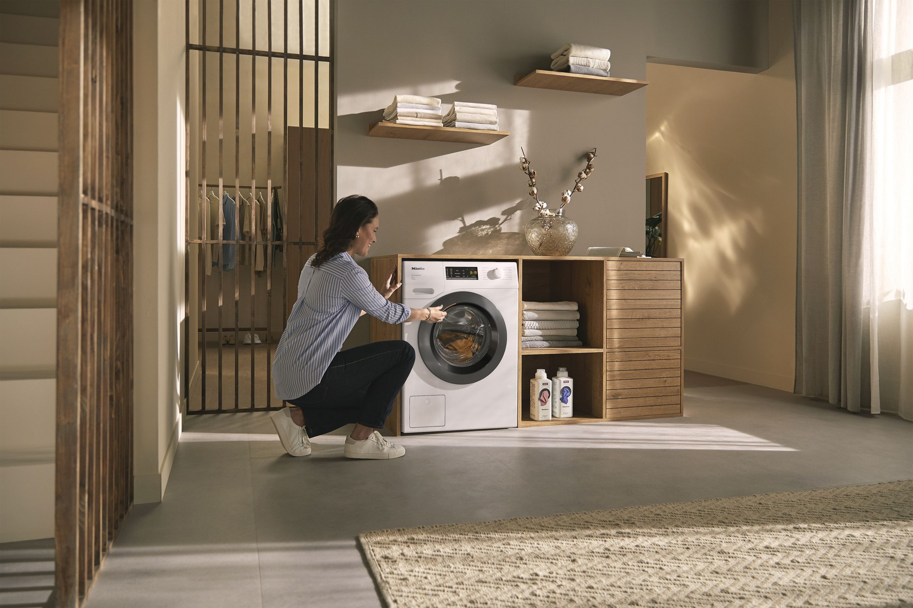 Donna inginocchiata vicino alla lavatrice, apre l'oblò. Ambiente lavanderia moderno.