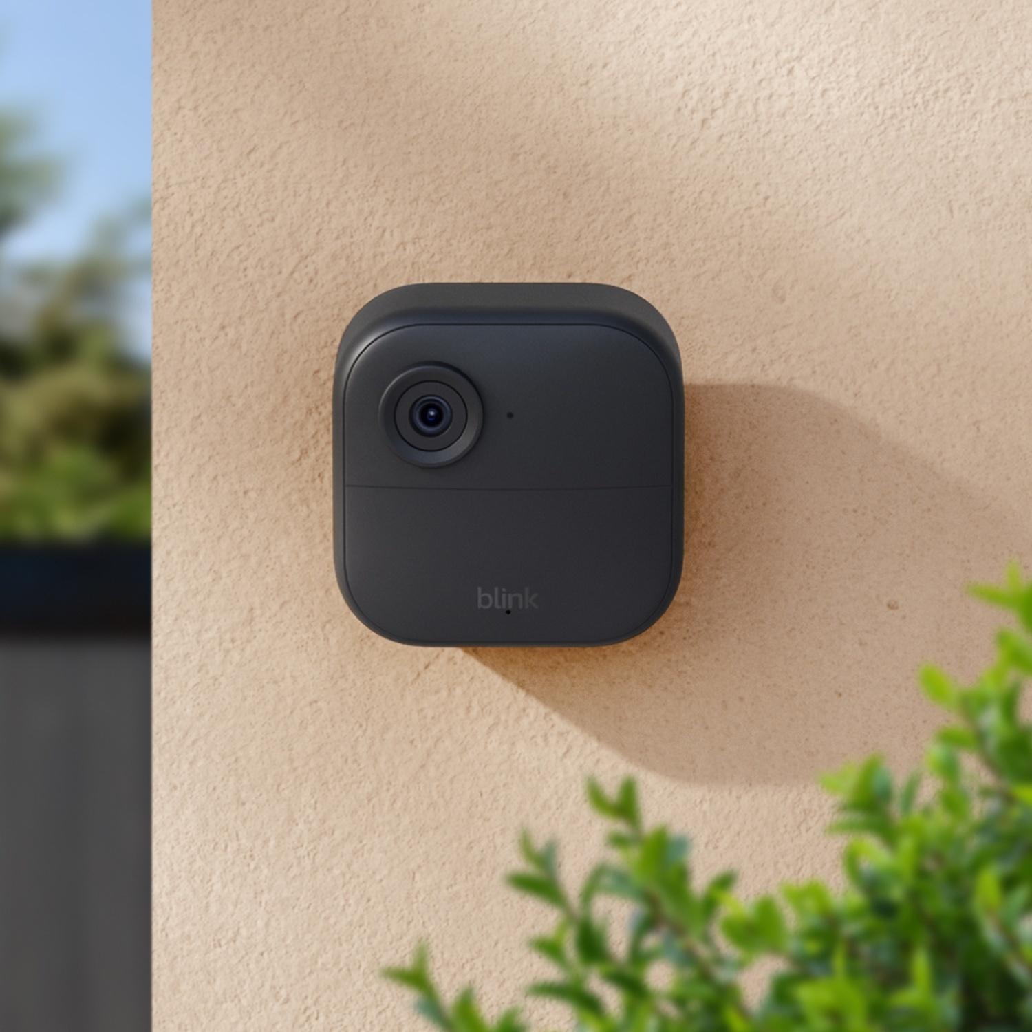 Eine schwarze Blink-Kamera ist an einer hellbeigen Wand montiert.