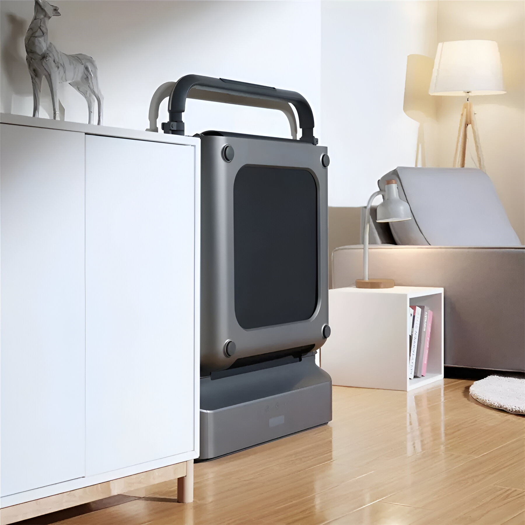 Szara bieżnia stoi obok białej szafki i sofy.