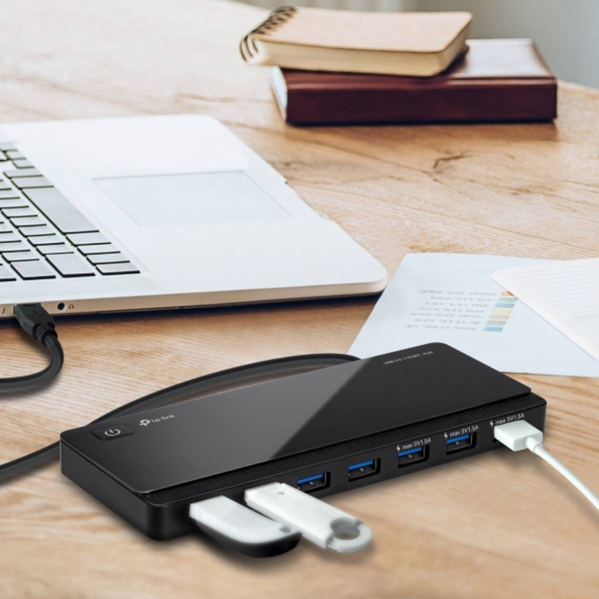 Schwarzer USB-Hub mit angeschlossenem Laptop und USB-Sticks auf einem Holztisch.