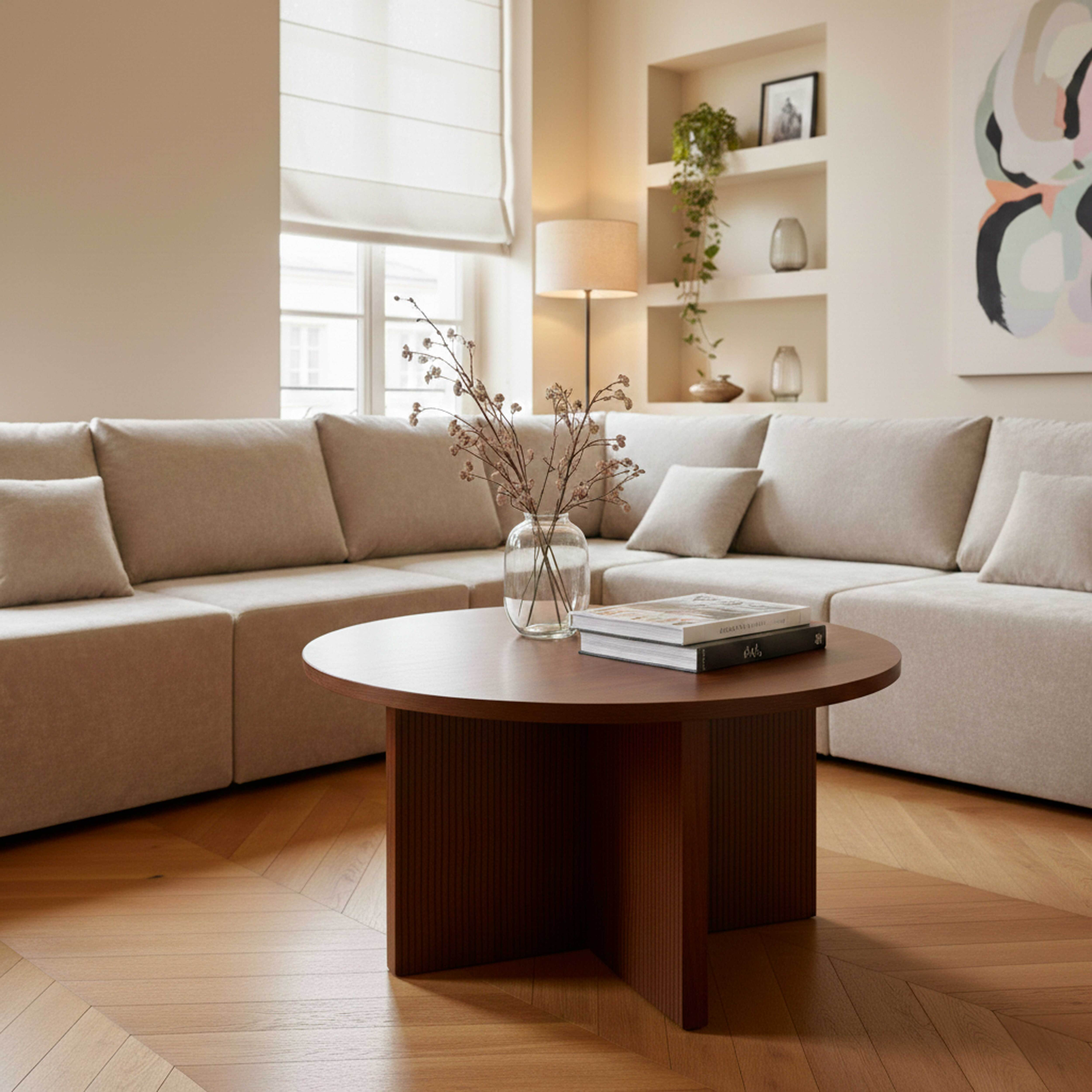 Ein helles Wohnzimmer mit einem Ecksofa, einem runden Holztisch und Büchern.