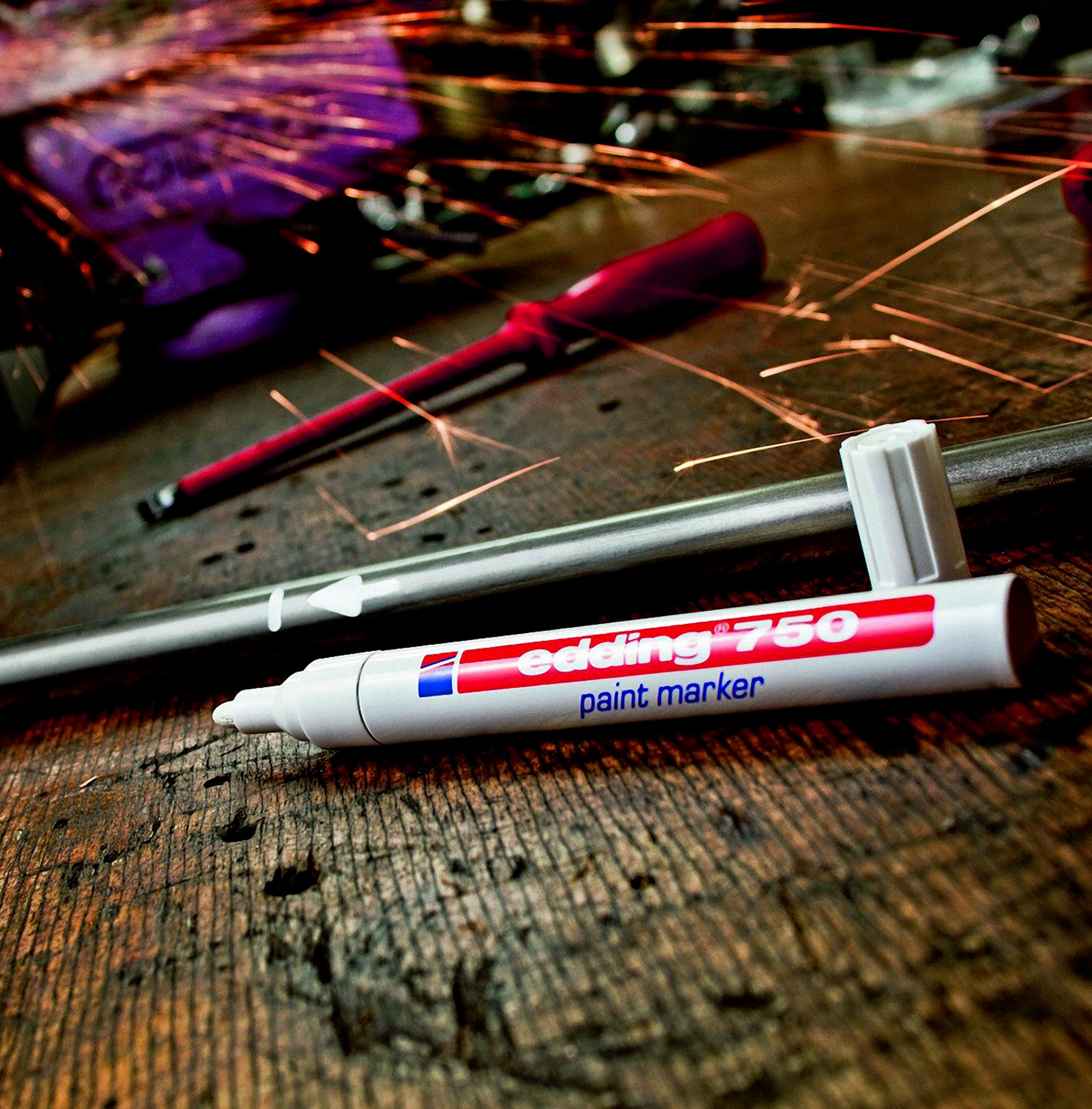 Ein Edding 750 Lackmarker liegt auf Holz. Funken fliegen im Hintergrund.